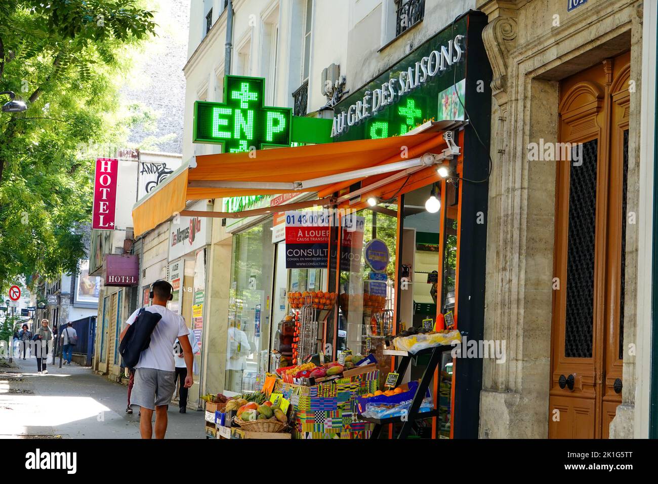 Mann in Fitnesskleidung, der am Obst- und Gemüsemarkt und der Apotheke vorbeigeht, Straßenszene, Alesia, 14. Arrondissement, Paris, Frankreich. Stockfoto