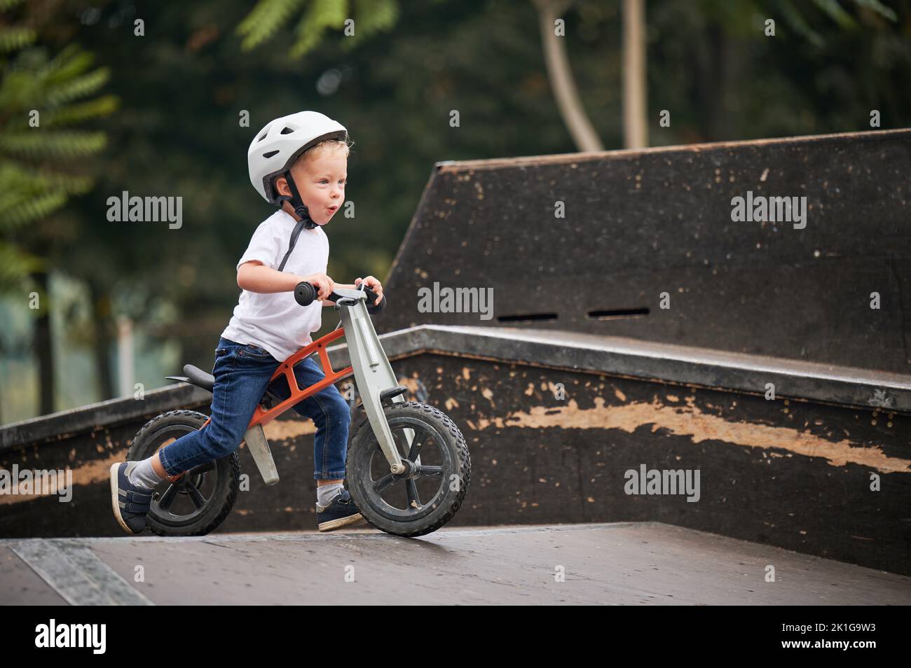Kind reitet Laufrad. Männliches Kleinkind im Helm, das im Skatepark lernt, auf dem Laufrad zu fahren. Stockfoto