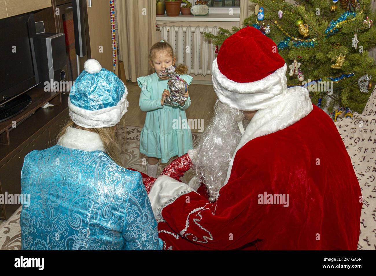 Eltern in festlichen Kostümen gratulieren ihrem Kind zu Froher Christmas und Neujahr. Stockfoto