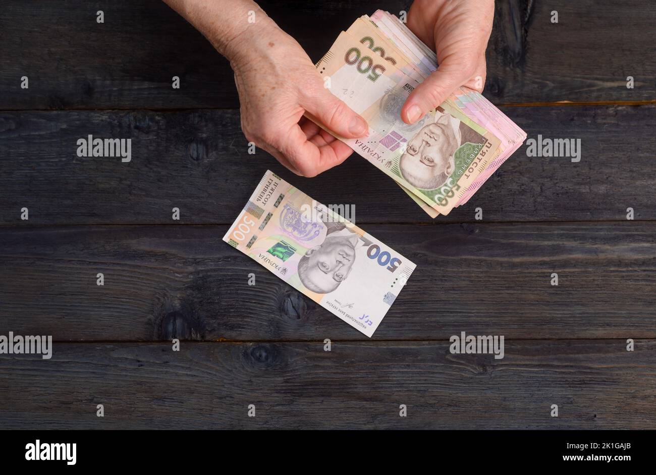 Eine ältere Frau zählt ihr Geld auf einem Holztisch Stockfoto