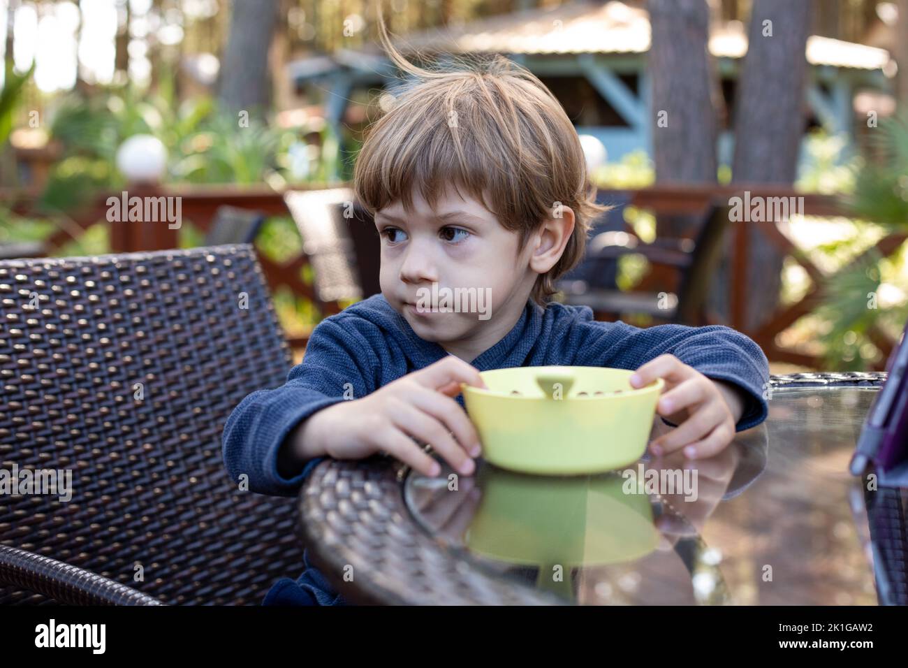 Der hübsche kleine Junge sitzt auf einem Stuhl am Tisch im Café auf der