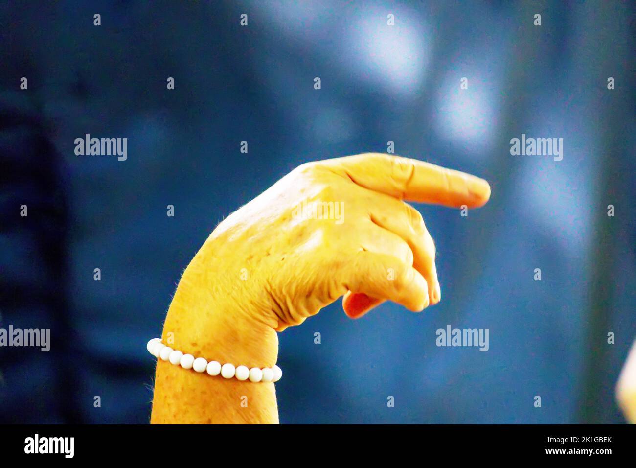 Ein Foto einer menschlichen Hand mit einem weißen Perlenarmband und einem dunkelblauen Hintergrund Stockfoto