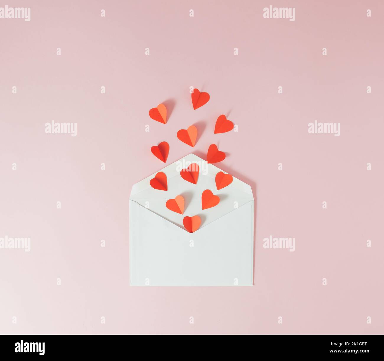 Rote Papierherzen fliegen aus einem weißen Umschlag - Valentinskarte. Minimalkonzept. Stockfoto