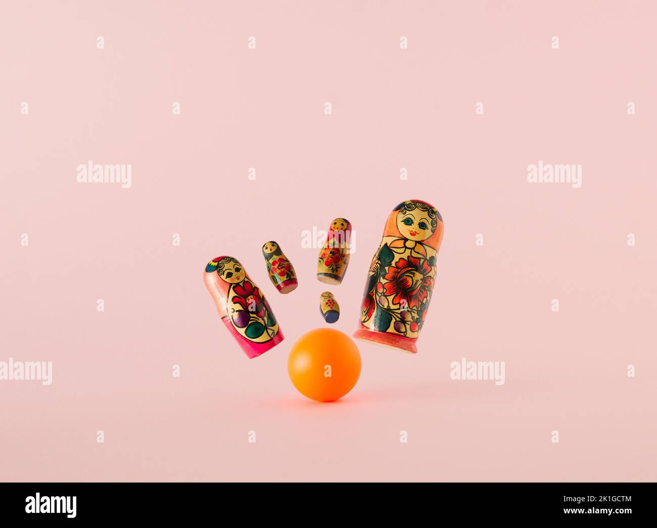 Russische Puppen, die als matryoshka oder babushka bekannt sind, als die Nadeln, die aus dem Schlag der orangefarbenen Bowlingkugel auf einem rosa Hintergrund fliegen. Minimalkonzept. Stockfoto