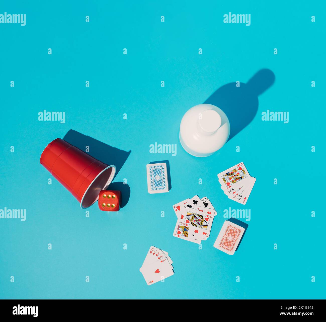 Pokerspiel mit frostigen Karten, roten Würfeln, rotem Plastikbecher und weißer Flasche auf blauem Hintergrund. Minimalkonzept. Stockfoto