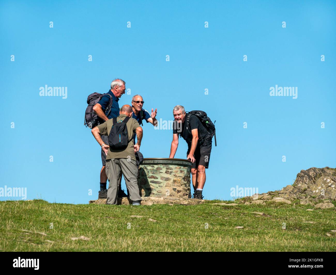 Gruppe von erwachsenen männlichen Wanderern / Spaziergängern in Shorts & Wanderstiefeln mit Rucksäcken, die Toposkop, Bradgate Park Hill, Leicestershire, England, Großbritannien, betrachten Stockfoto