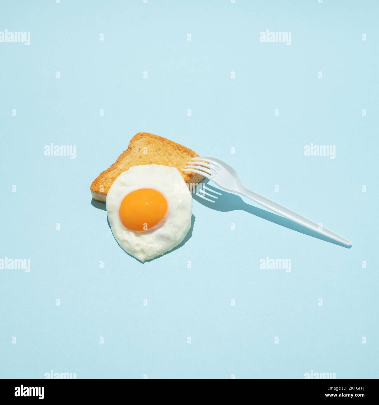 Gebratenes Ei auf Toast mit weißer Kunststoffgabel. Minimales kreatives Lebensmittelkonzept. Stockfoto