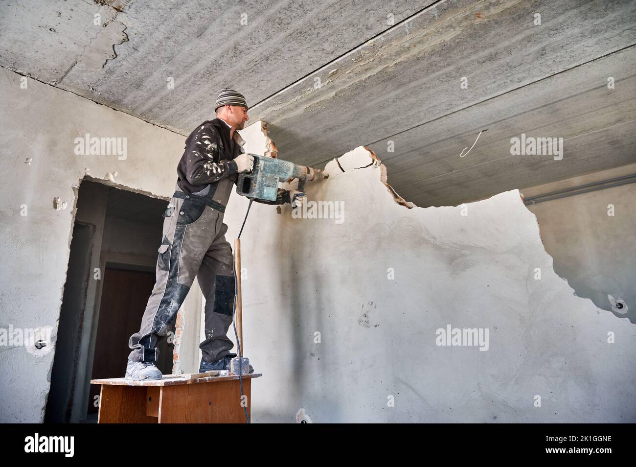 Niedrige Ansicht des Arbeiters mit dem Abbruchhammer, der die Zwischenwand bricht. Allgemeine Reparatur zu Hause mit einem Absturz der Wand trennt zwei Zimmer für die Schaffung eines großen Wohnzimmer. Stockfoto