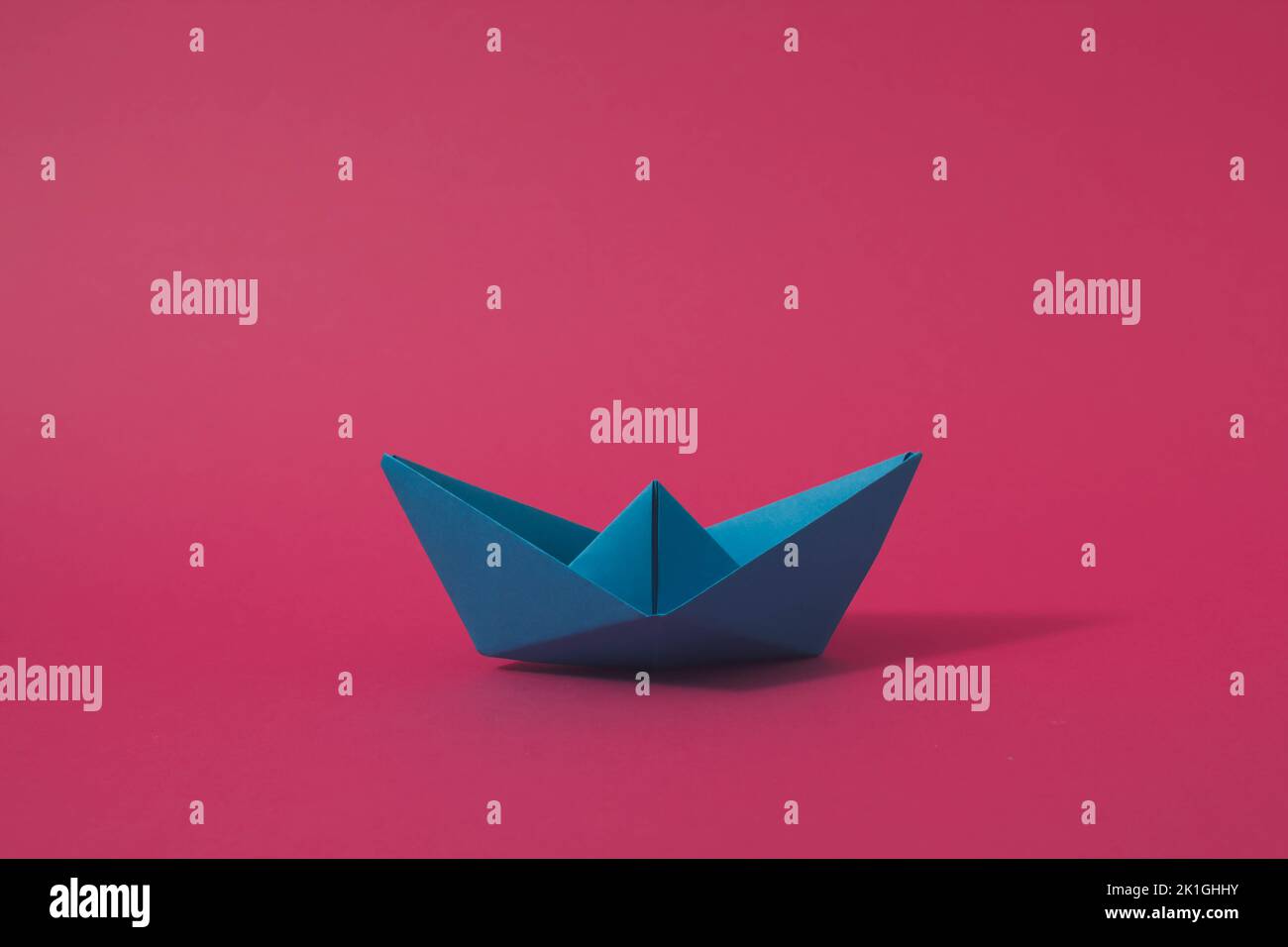 Blaues Origami-Papier Boot auf rosa Hintergrund. Minimalkonzept. Stockfoto