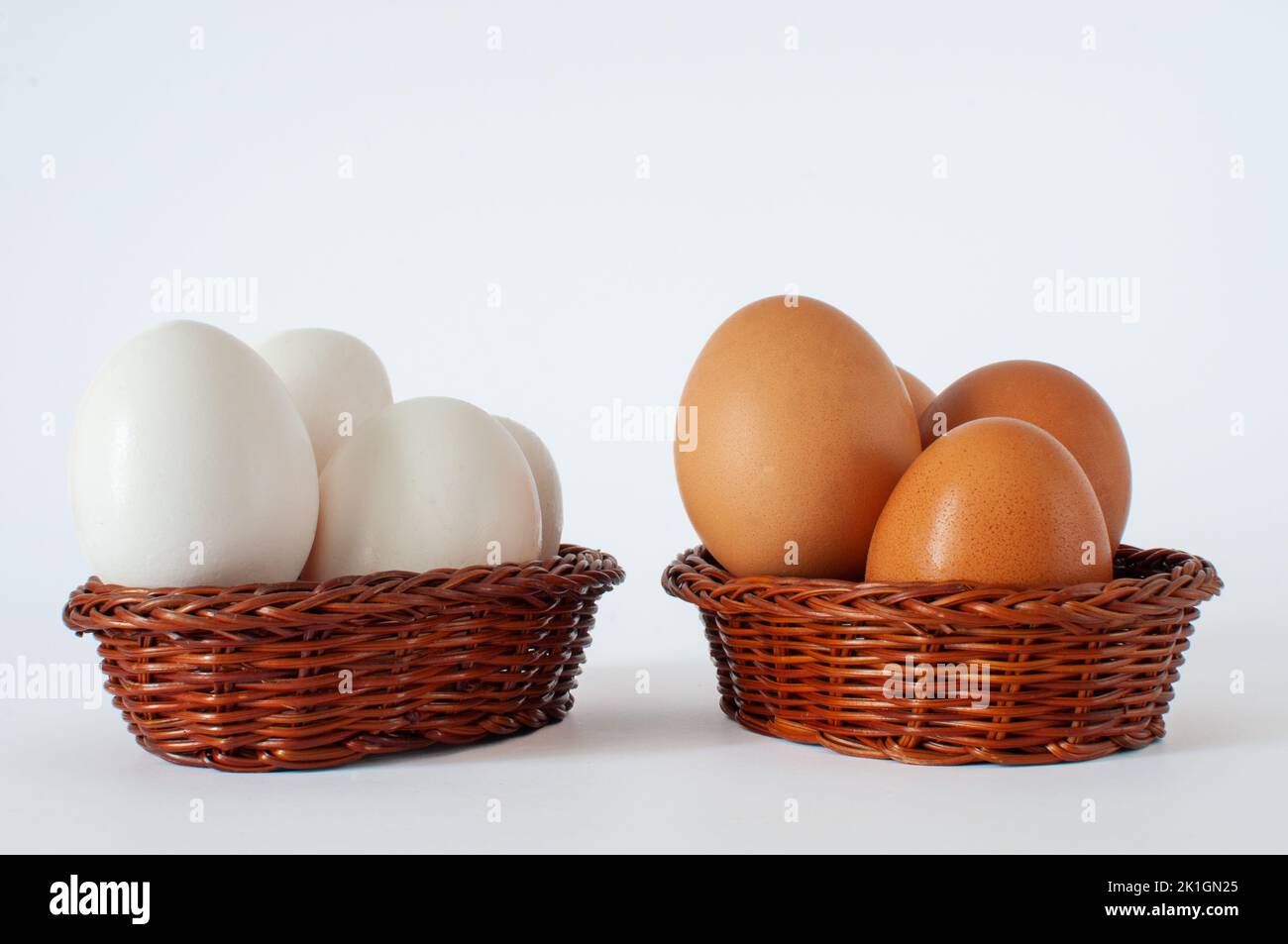 Braune und weiße Hühnereier in braunen Mini-Körben, isoliert auf weißem Hintergrund. Legen Sie nicht alle Ihre Eier in einem Korb Idee Konzept. Stockfoto