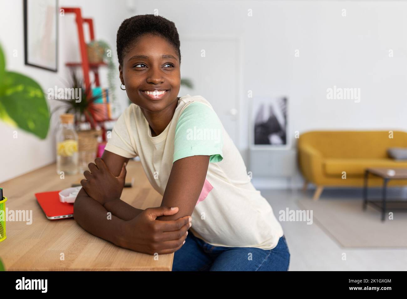 Porträt einer verträumten afrikanischen jungen Frau, die im modernen Heimstudio am Schreibtisch sitzt Stockfoto