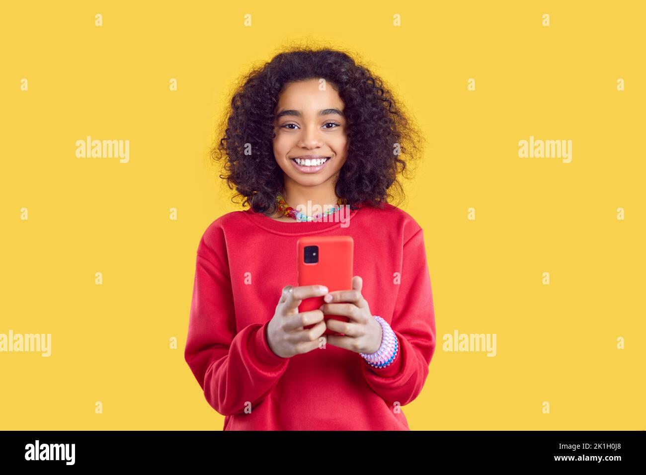 Lächelndes, ethnisches Mädchen nutzt ein modernes Mobiltelefon für Online-Spiele oder zur Kommunikation mit Freunden Stockfoto