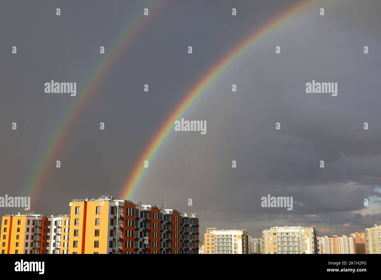 Doppelter Regenbogen über Stadtgebäuden nach Regen auf dem Hintergrund des Sturmhimmels Stockfoto