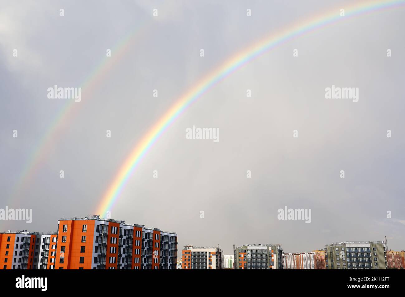 Doppelter Regenbogen über Stadtgebäuden nach Regen auf dem Hintergrund des Sturmhimmels Stockfoto