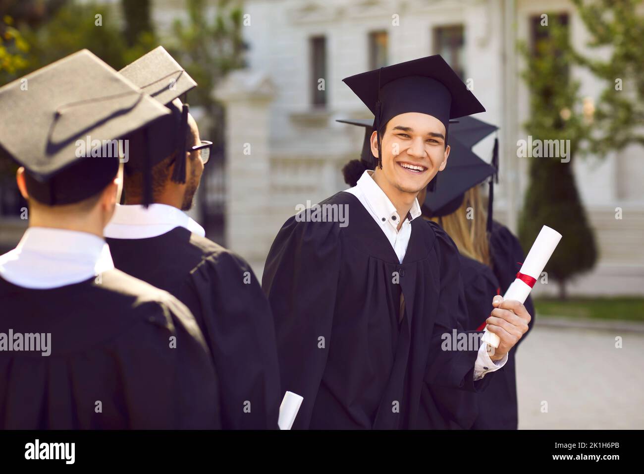 Fröhlicher Universitätsstudent in seiner Mütze und seinem Kleid, der sich am Abschlusstag amüsieren konnte Stockfoto