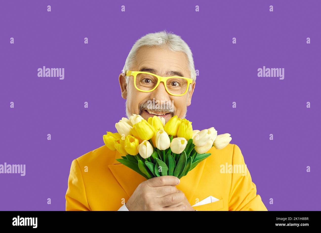 Portrait von fröhlichen niedlichen alten Mann mit Strauß von gelben Tulpen auf lila Hintergrund. Stockfoto