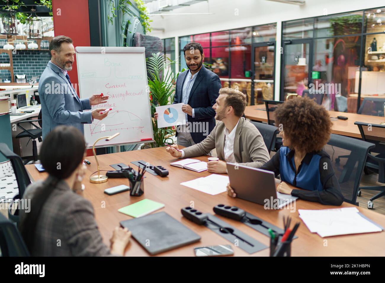 Ein reifer Business Coach oder Redner präsentiert den verschiedenen Geschäftsleuten auf einem Flipchart-Blatt Stockfoto