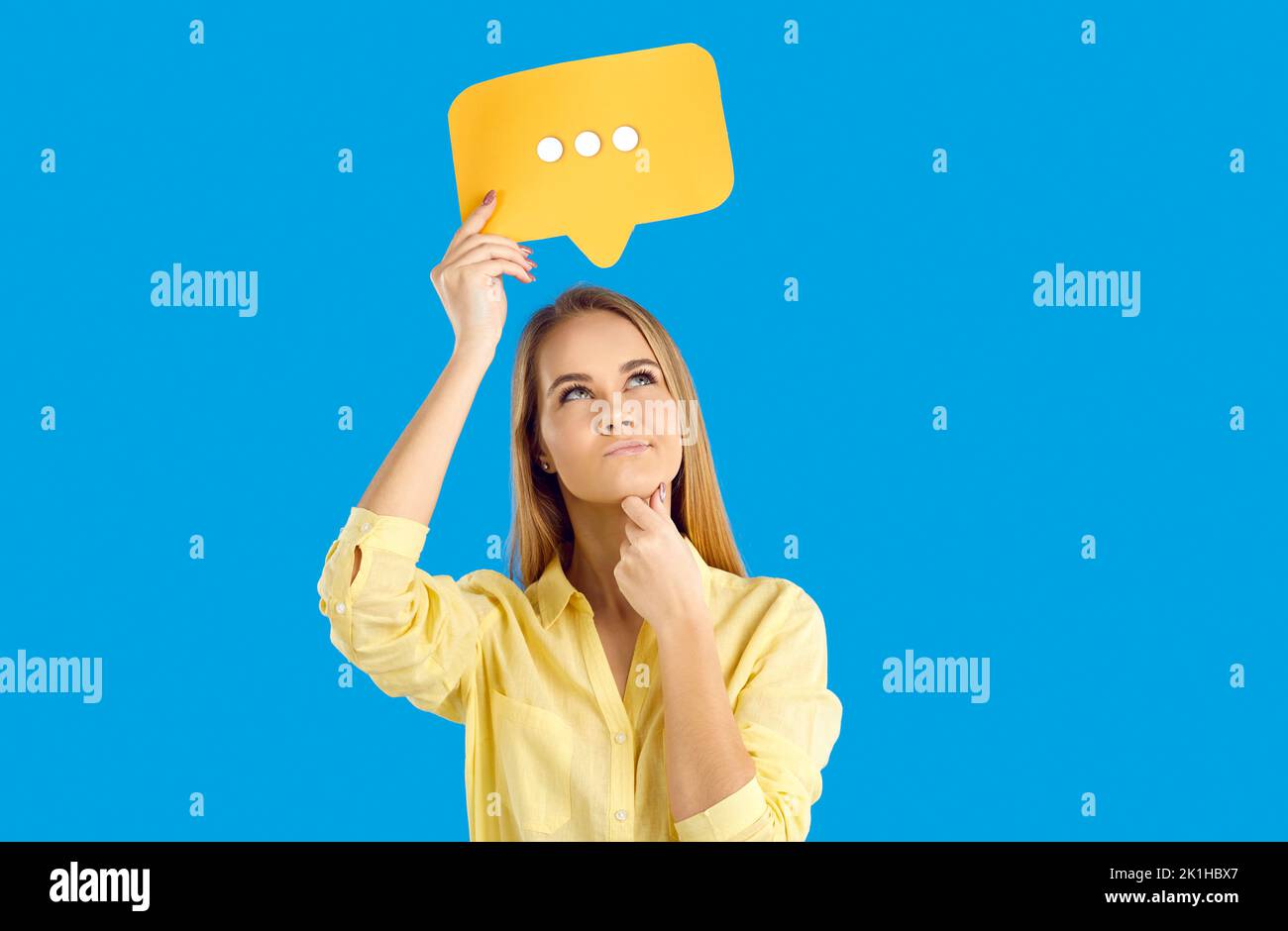 Junge Frau mit Symbol für soziale Kommunikation in den Händen, die im Chat über Antworten nachdenkt. Stockfoto