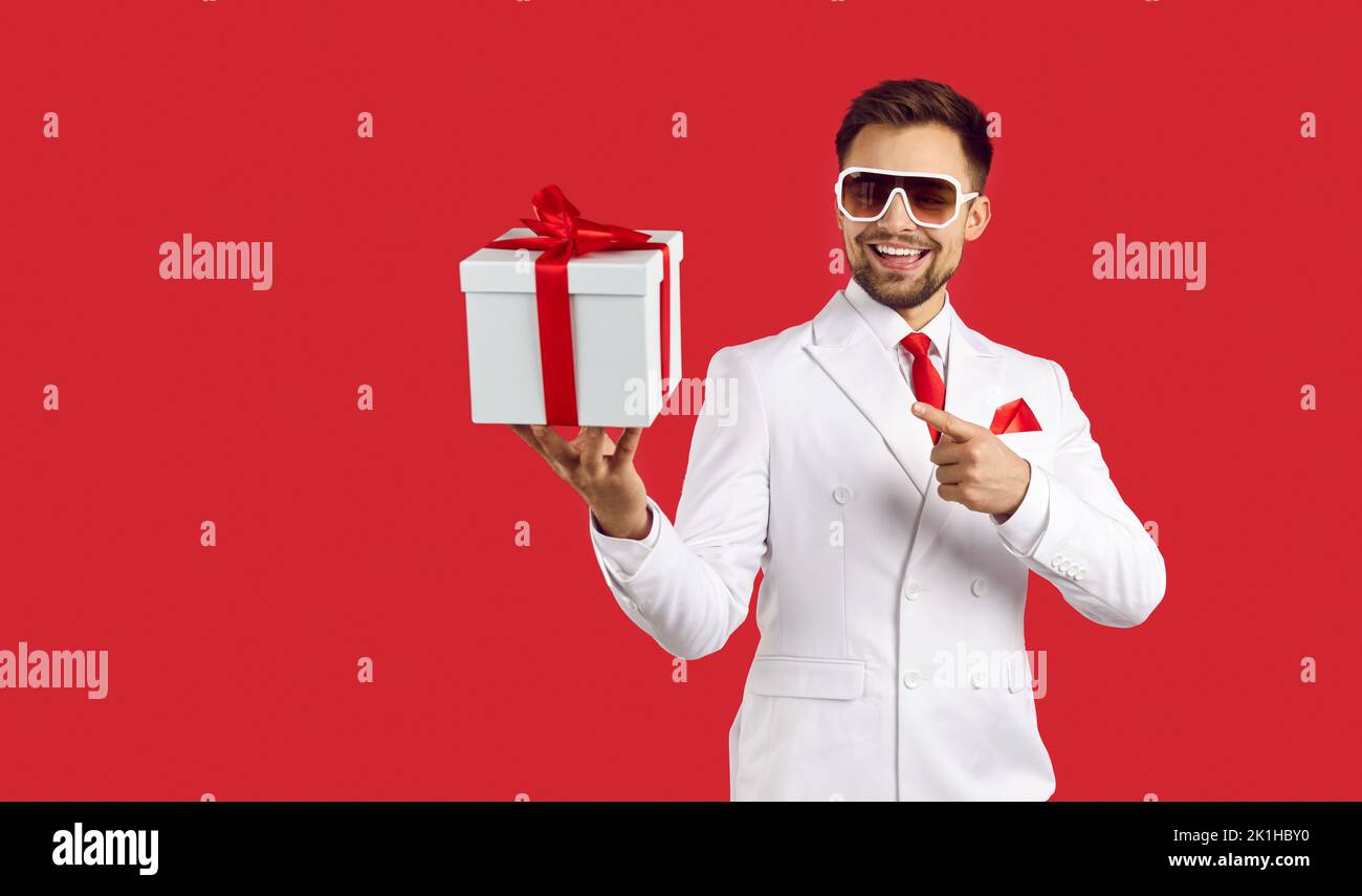 Glücklicher, gutaussehender Mann in Anzug und Brille, lächelnd und mit dem Hinweis auf die Geschenkbox in der Hand Stockfoto