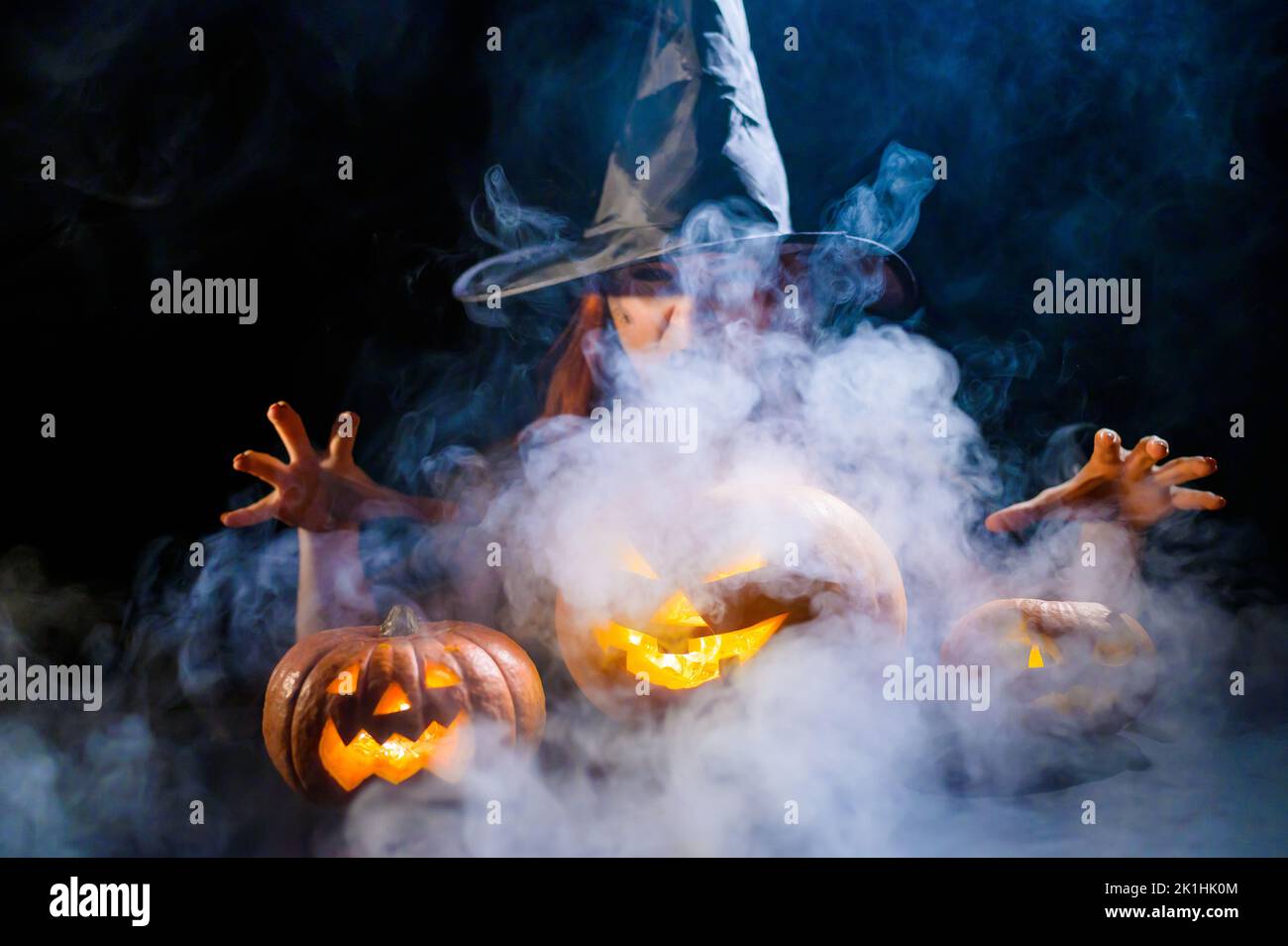 Eine ominöse Hexe im Hut zaubert über eine Jack-o-Laterne. Traditionelle halloween-Figuren 