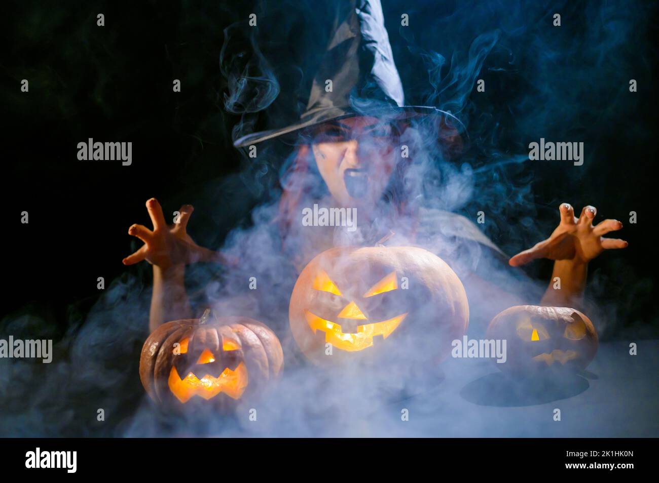 Eine ominöse Hexe im Hut zaubert über eine Jack-o-Laterne. Traditionelle halloween-Figuren 