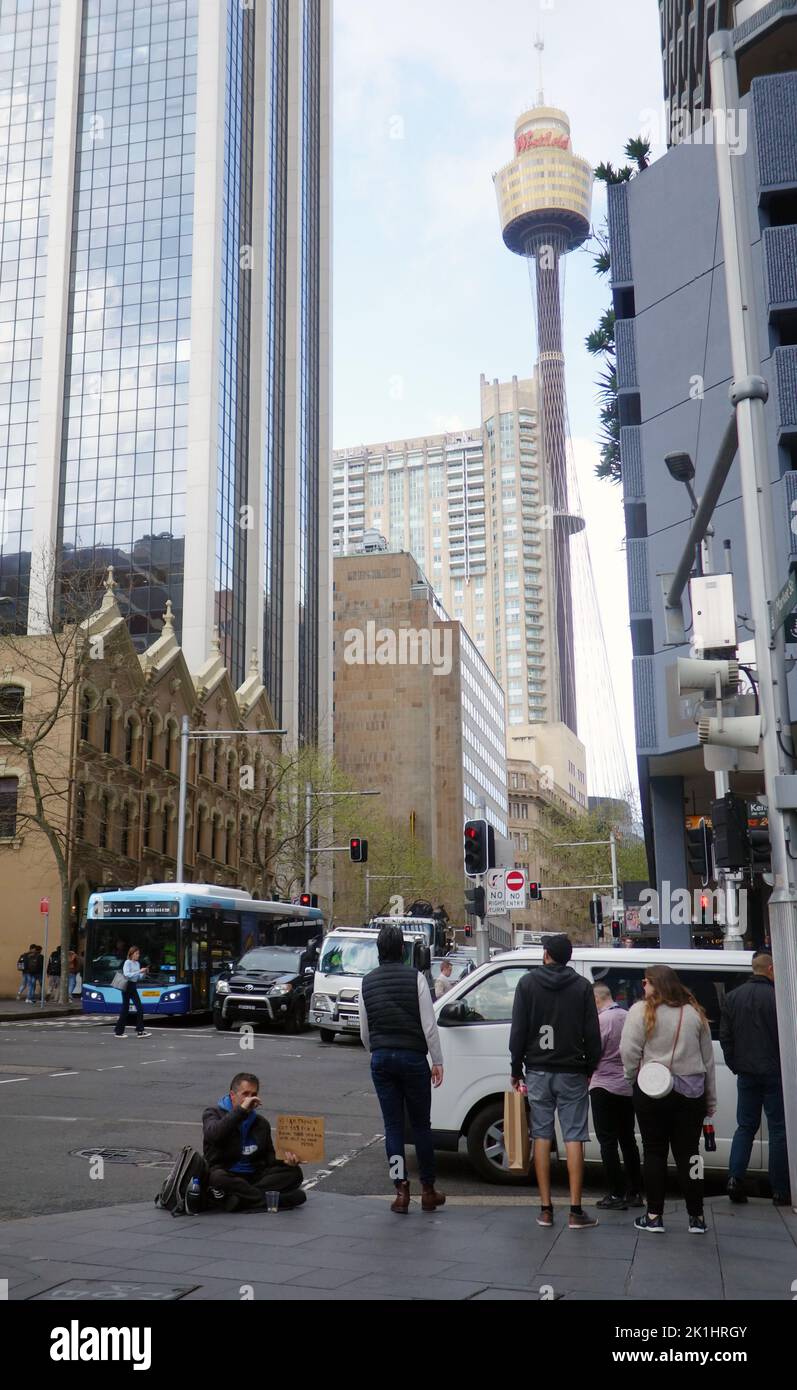 Obdachloser Mann mit Schild, der um Geld bat, mit Centerpoint Tower im Hintergrund, Sydney CBD, NSW, Australien. Nein, MR Stockfoto