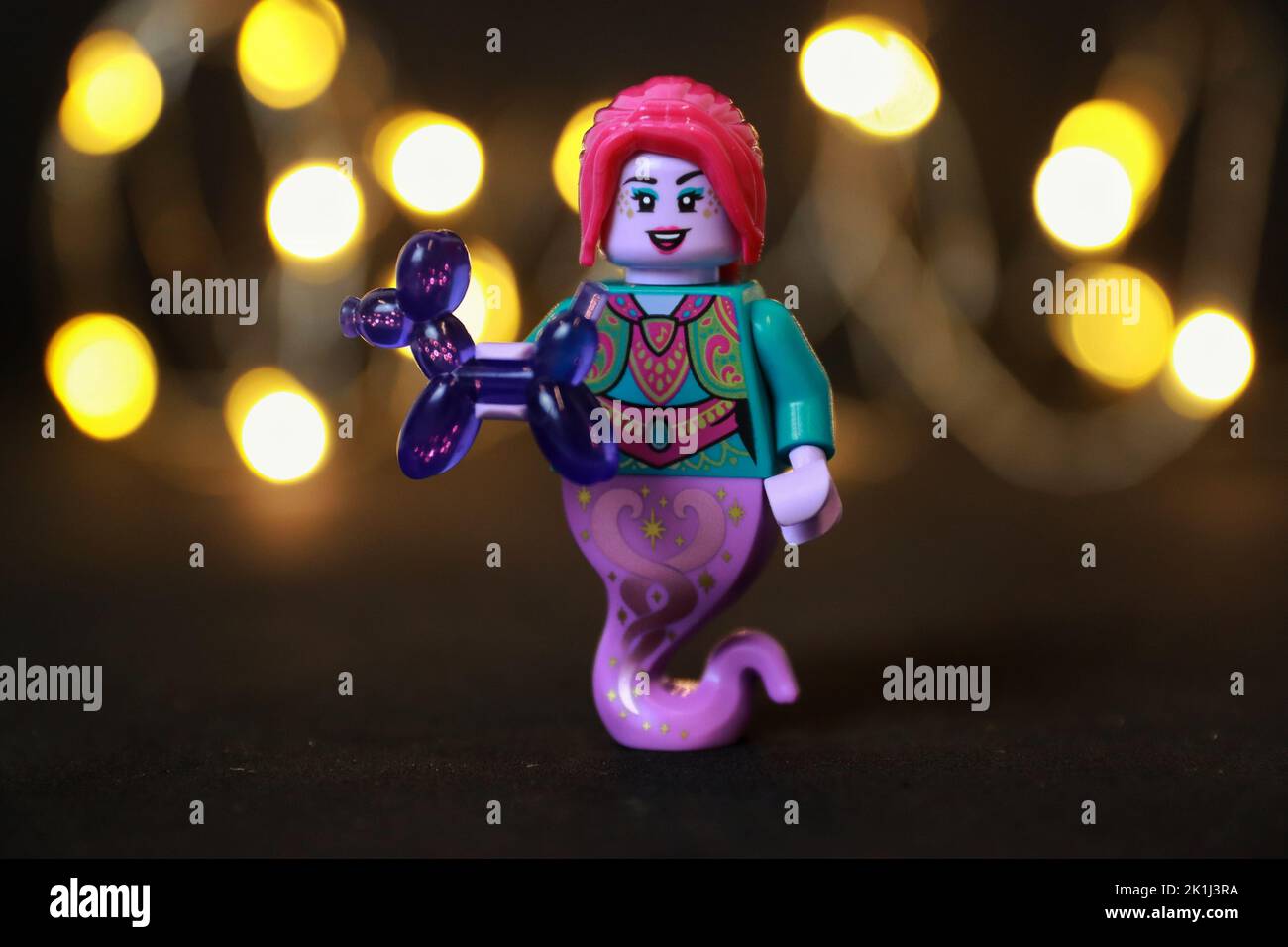 Eine weibliche Spielzeugfigur mit roten Haaren und Lippen, die ein violettes Ballontier hält Stockfoto