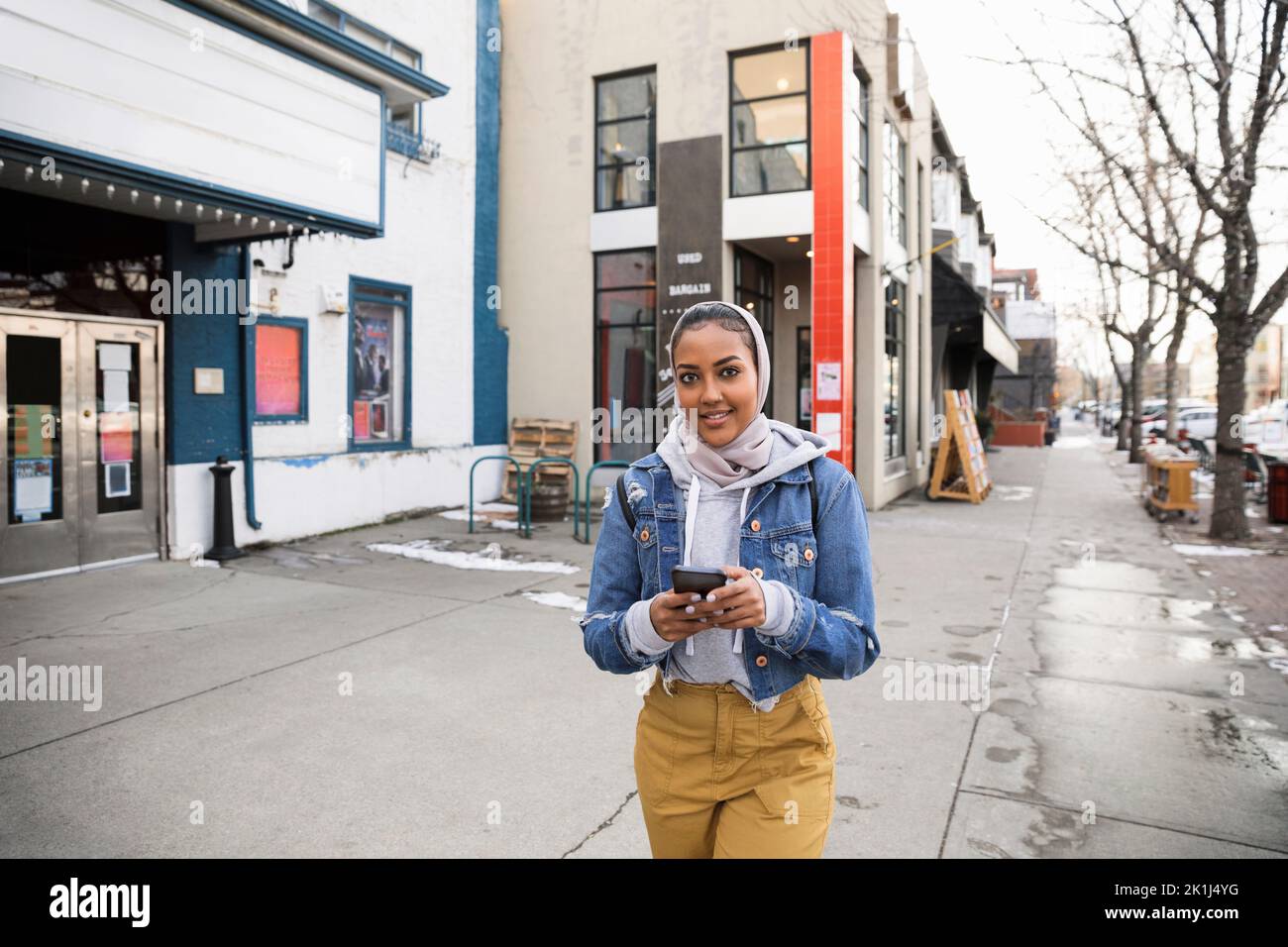Portrait selbstbewusste junge Frau im Kopftuch mit Smartphone außerhalb des Kinos Stockfoto