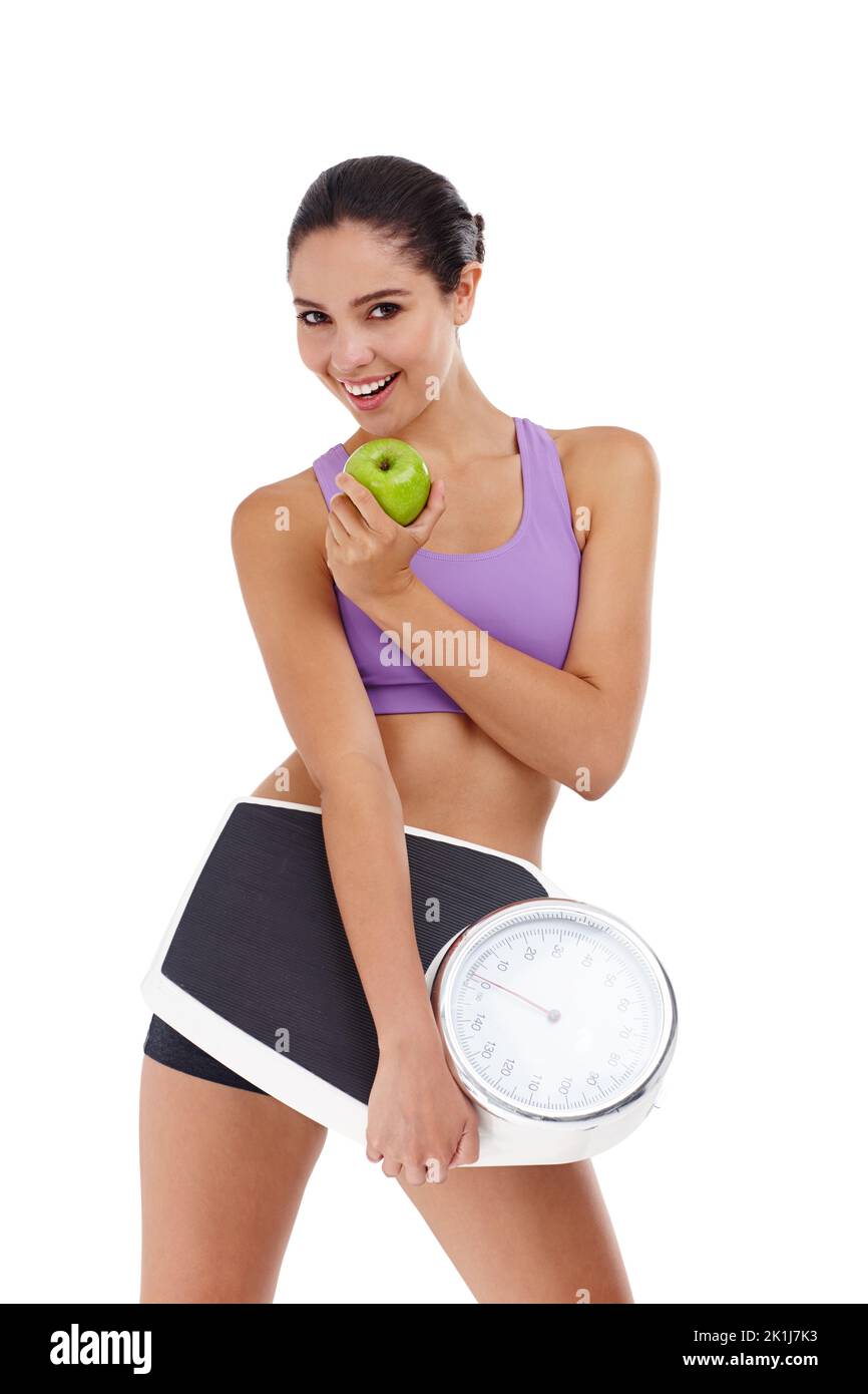 Essen gesund für den Sommer Körper. Studioaufnahme einer attraktiven jungen Frau in Turnkleidung mit Apfel- und Waage. Stockfoto
