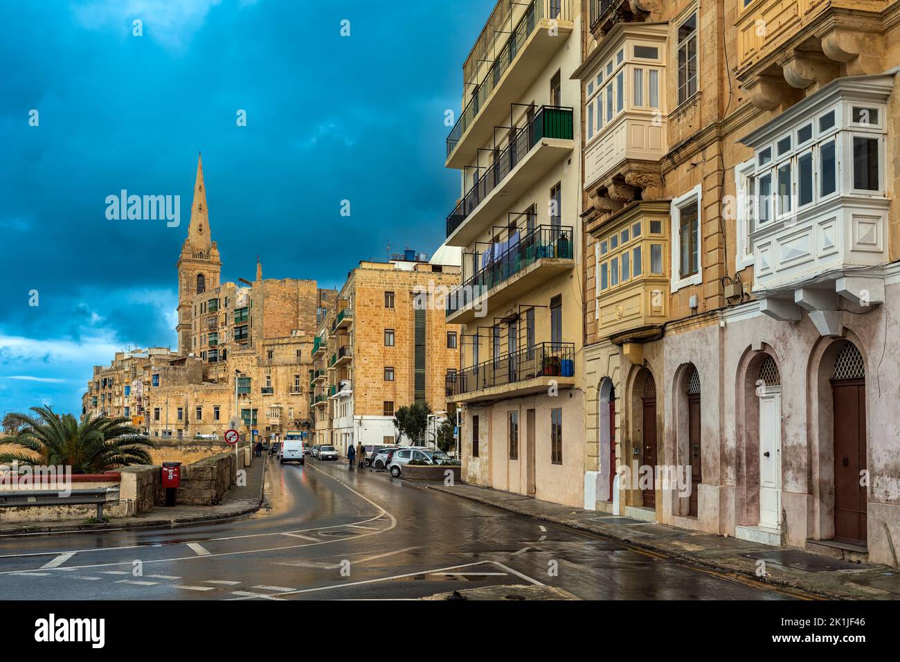 Typisches Wohngebäude und die nasse Stadtstraße unter schönem, wolkig-stürmischen Himmel in Valletta, Malta. Stockfoto