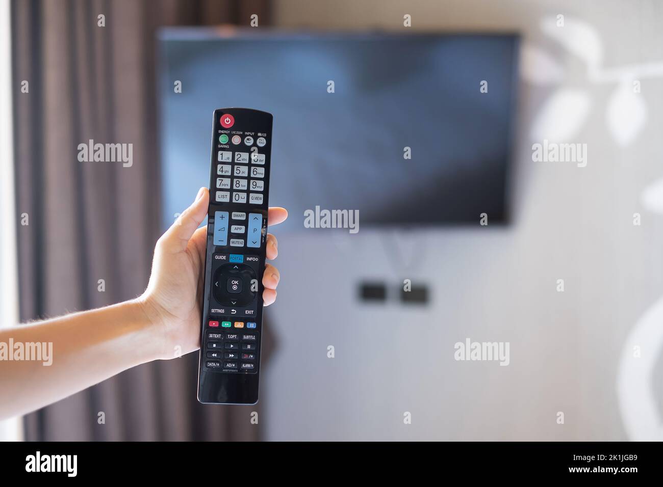 Hand mit Fernbedienung für Smart TV im modernen Zimmer zu Hause oder in einem Luxushotel einstellen Stockfoto