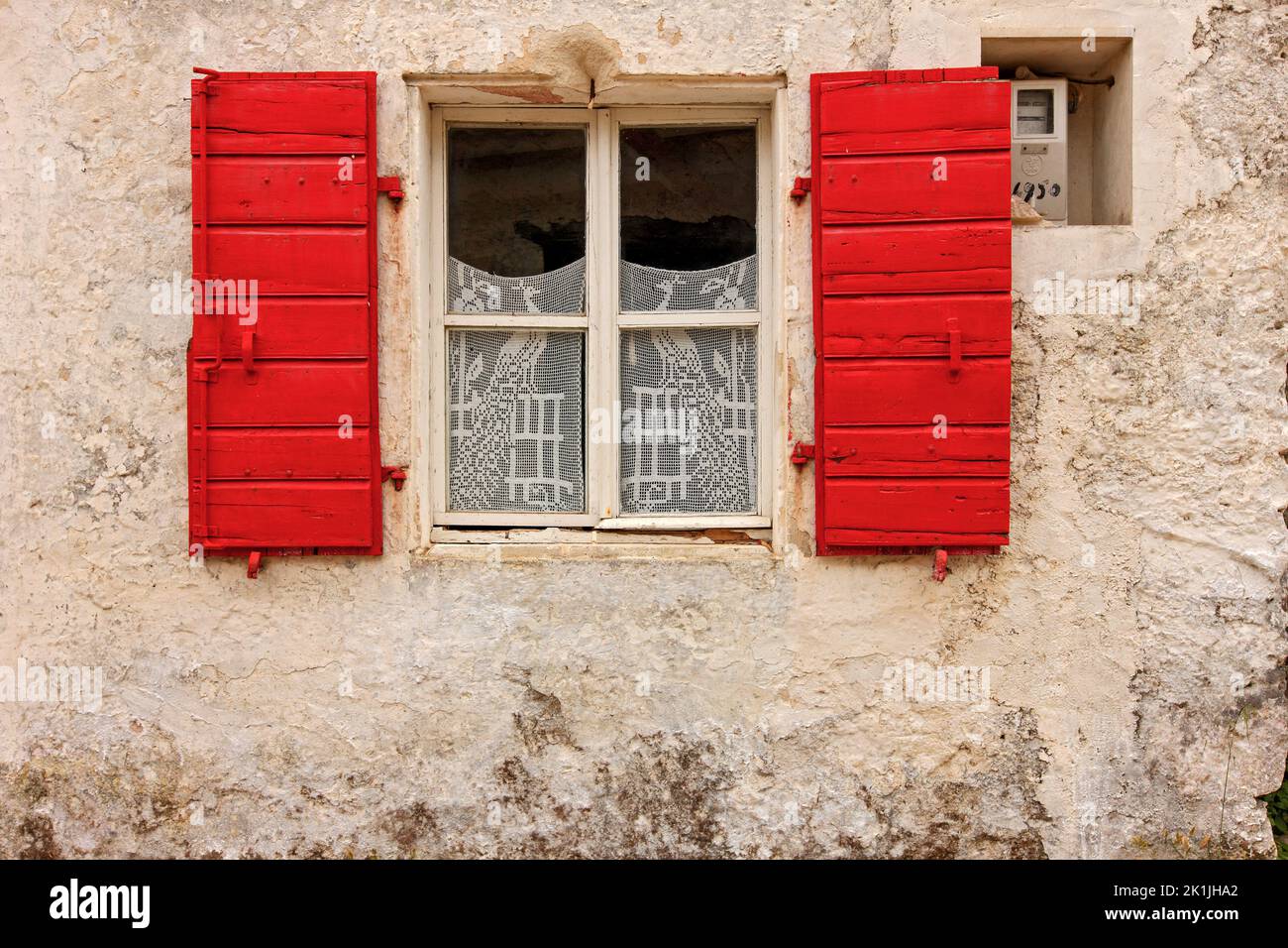 Malerische Fassade des traditionellen lokalen Hauses mit Steinmauer, rotem Fenster und aufwendigen Spitzenvorhängen, gesehen in einem Dorf der Insel Zakynthos, Griechenland Stockfoto