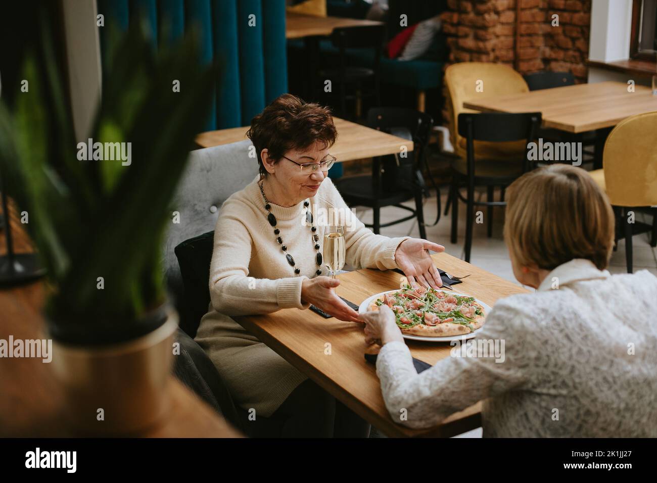 Zwei Freunde treffen sich und essen im Restaurant, alte, dressy Damen mit leckerem Pizza am Tisch im Café-Saal. Alte Freunde trinken Champagner Stockfoto