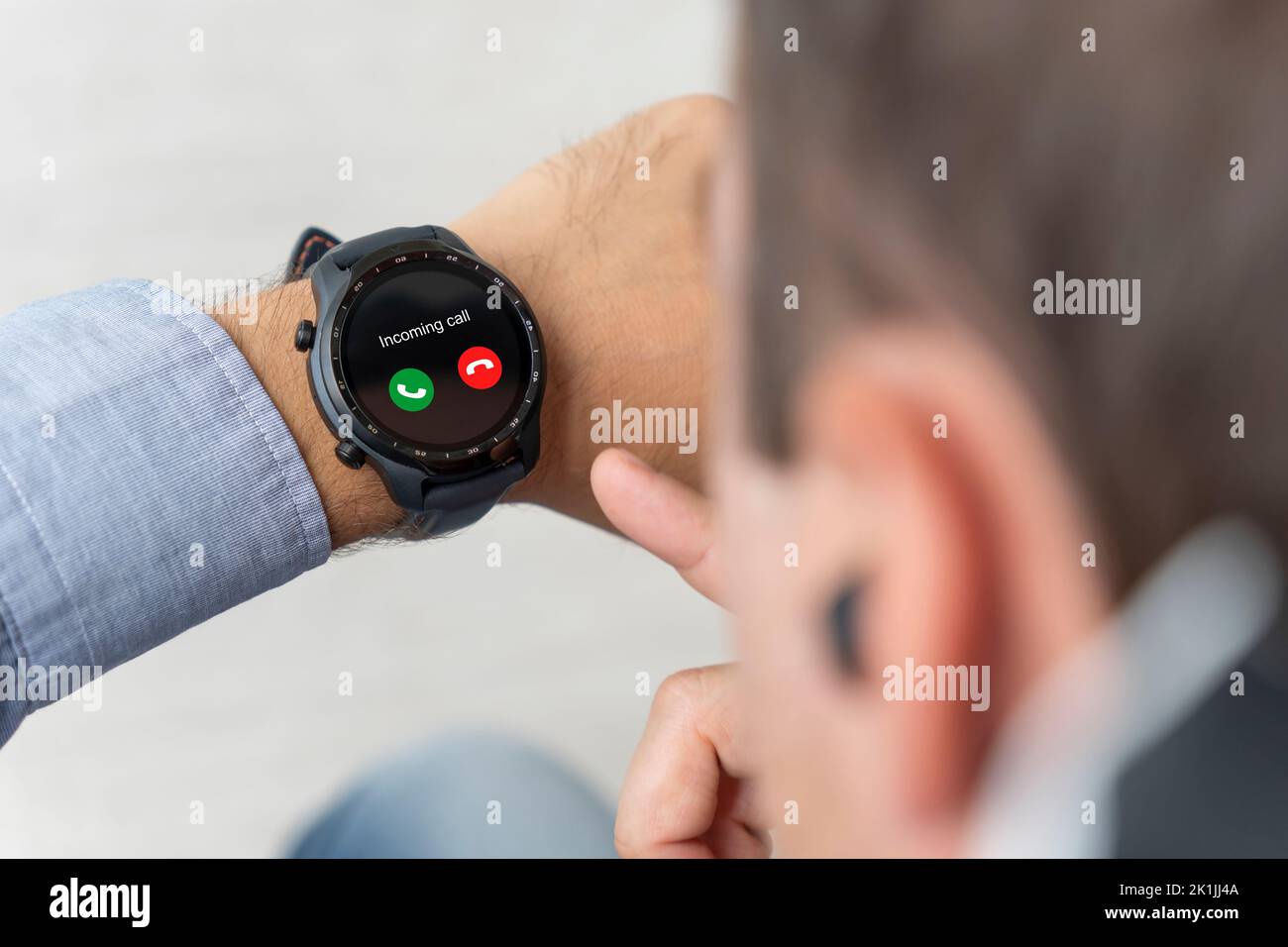 Attraktiver Mann, der auf die Uhr schaut, während er mit dem Smartphone spricht. Ankommender Anruf auf einer modernen Smart-Uhr. Der Typ drückt einen Knopf auf seiner Uhr. Stockfoto