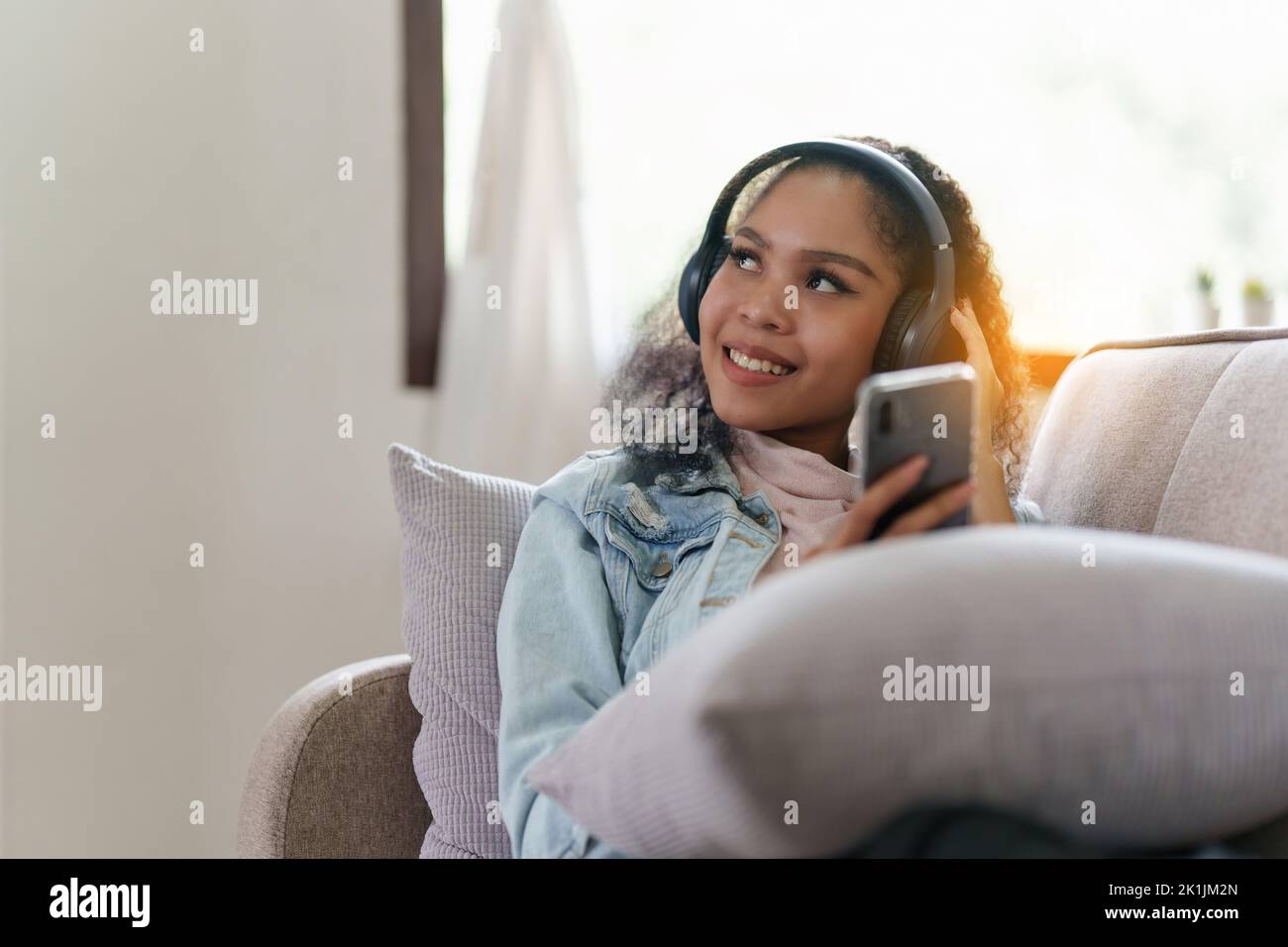 Attraktive lächelnde junge Frau mit Handy und Musik hören auf dem Sofa zu Hause. Lifestyle-Konzept Stockfoto