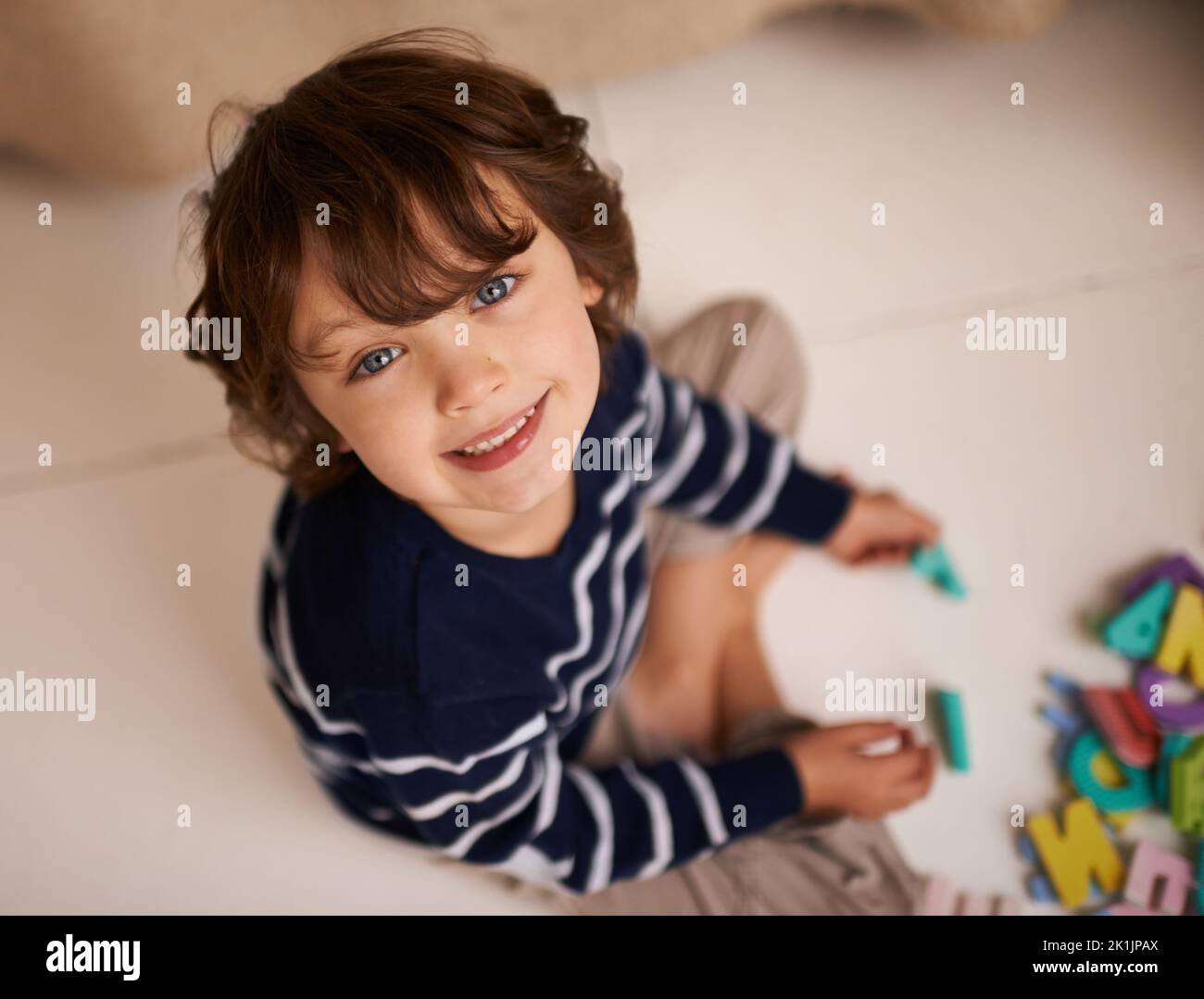 Genie im Training. Portrait eines entzückenden kleinen Jungen, der mit bunten Spielzeugbuchstaben spielt. Stockfoto