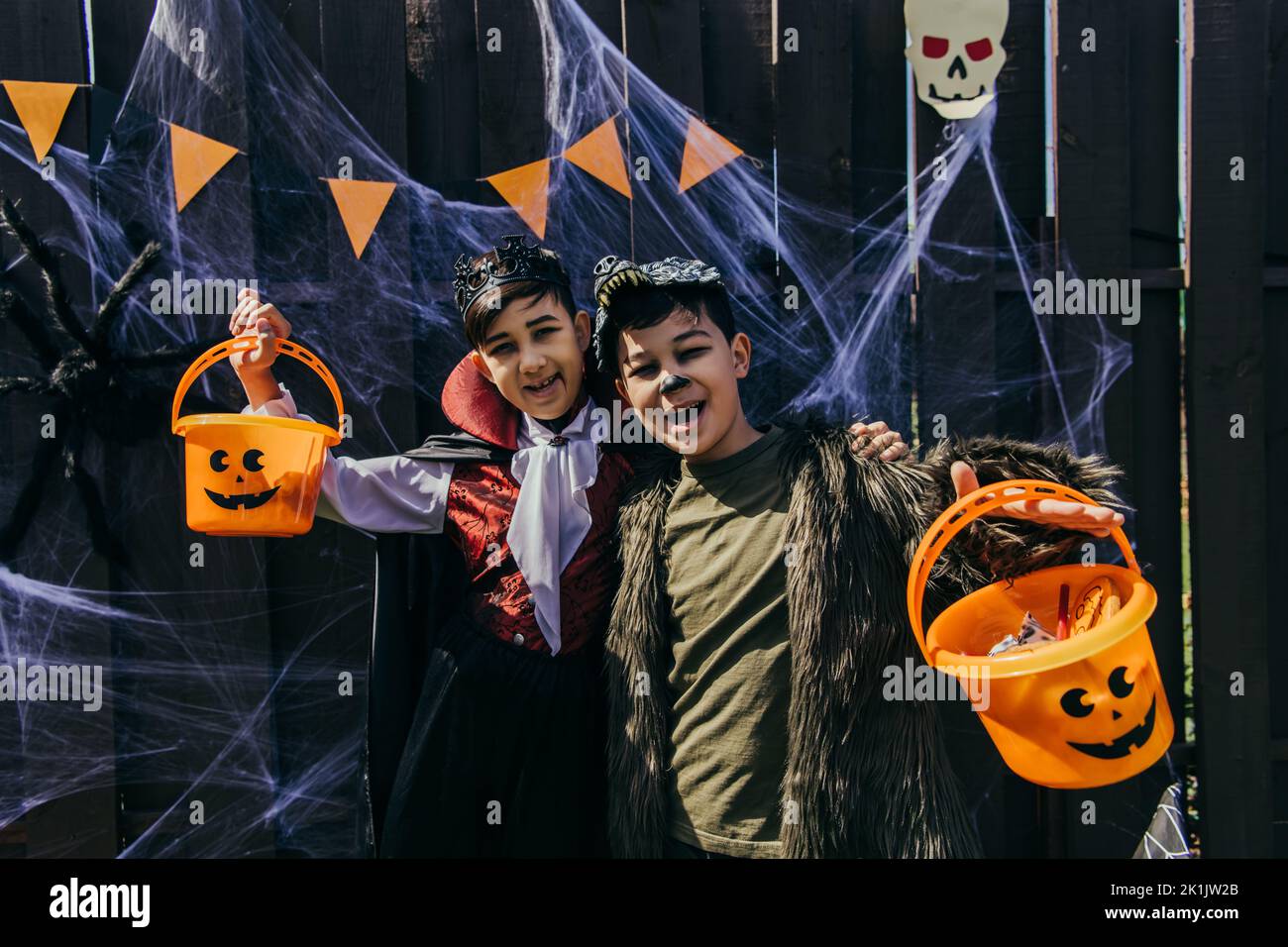 Asiatische Kinder halten halloween Eimer mit Süßigkeiten in der Nähe Spinnennetz auf Zaun während der Party im Hinterhof Stockfoto