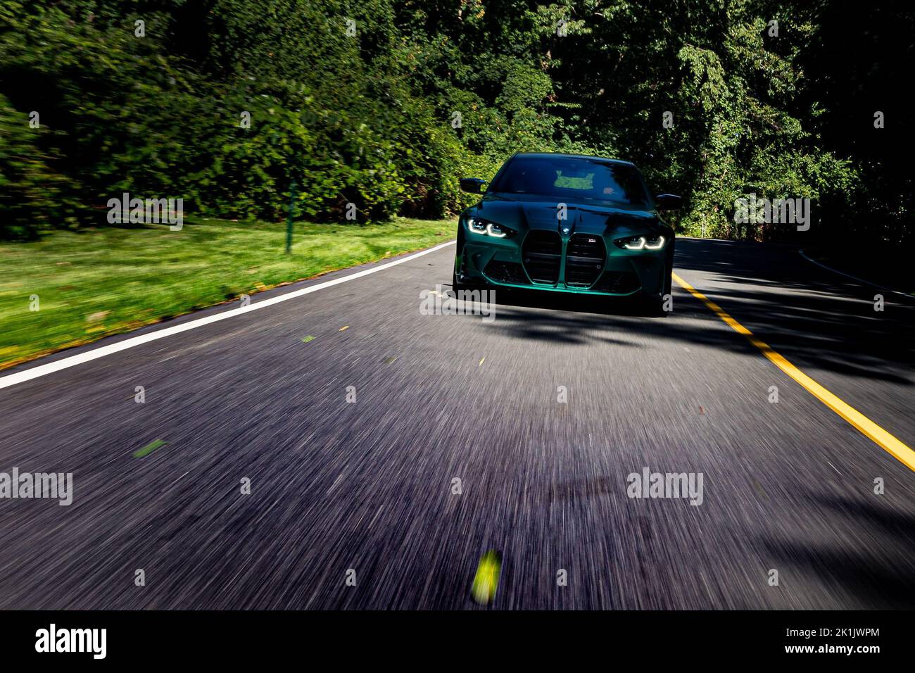 Rollende Aufnahme des BMW M4 Performance auf asphaltierter Straße mit verwischten Bäumen im Hintergrund Stockfoto