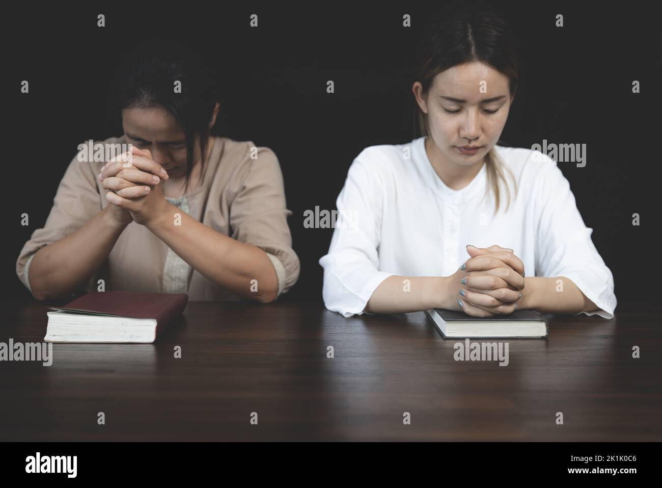 Zwei christliche Frauen sitzen zusammen und beten auf einem Holztisch mit verschwommenen, offenen Bibelseiten in ihrem Zimmer. Gebet für Brüder, Glaube, Hoffnung, Liebe, p Stockfoto