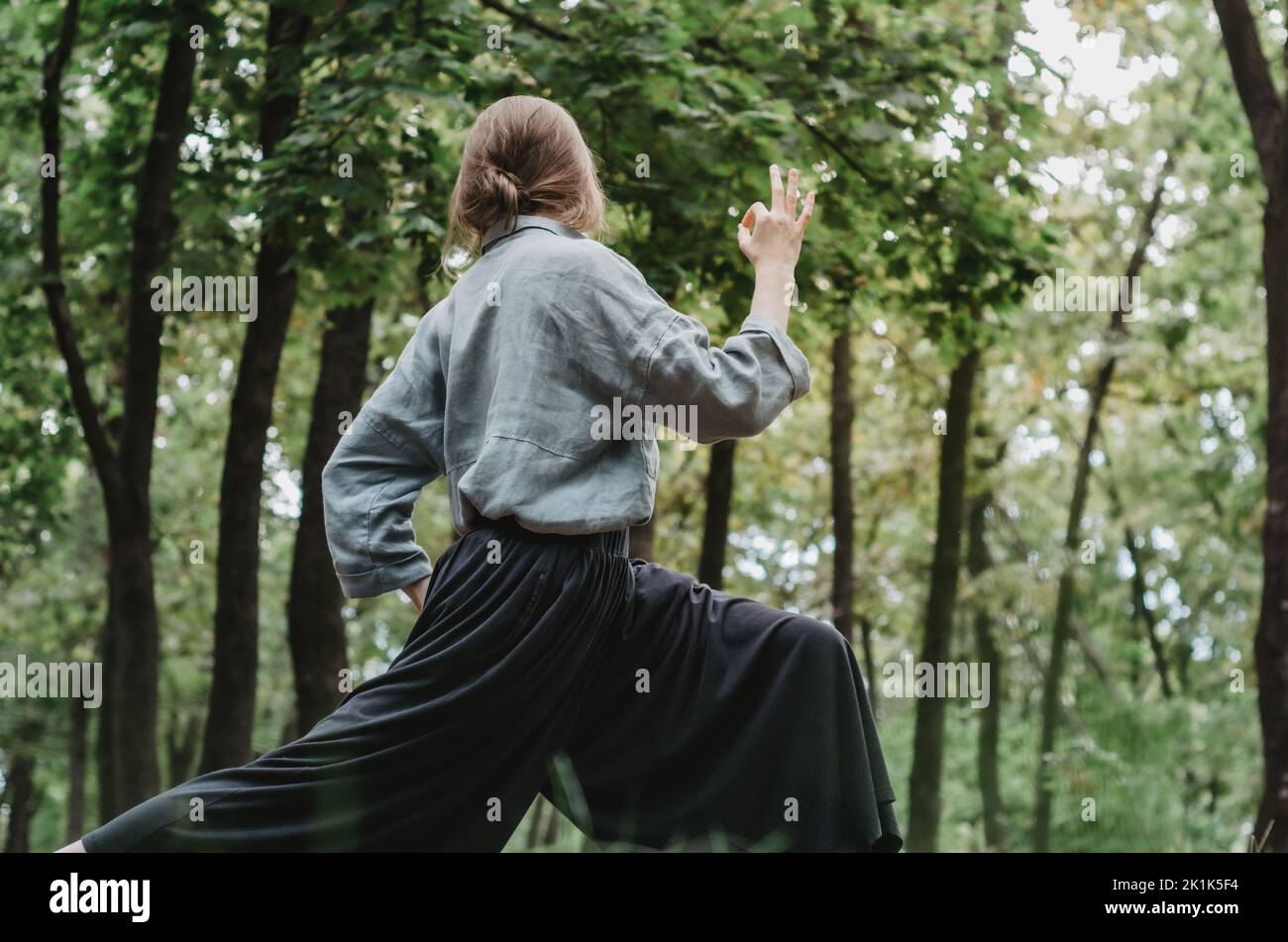 Frau in lockerer, bequemer Kleidung, die im Wald Yoga macht und ein Schild mit OK zeigt Stockfoto