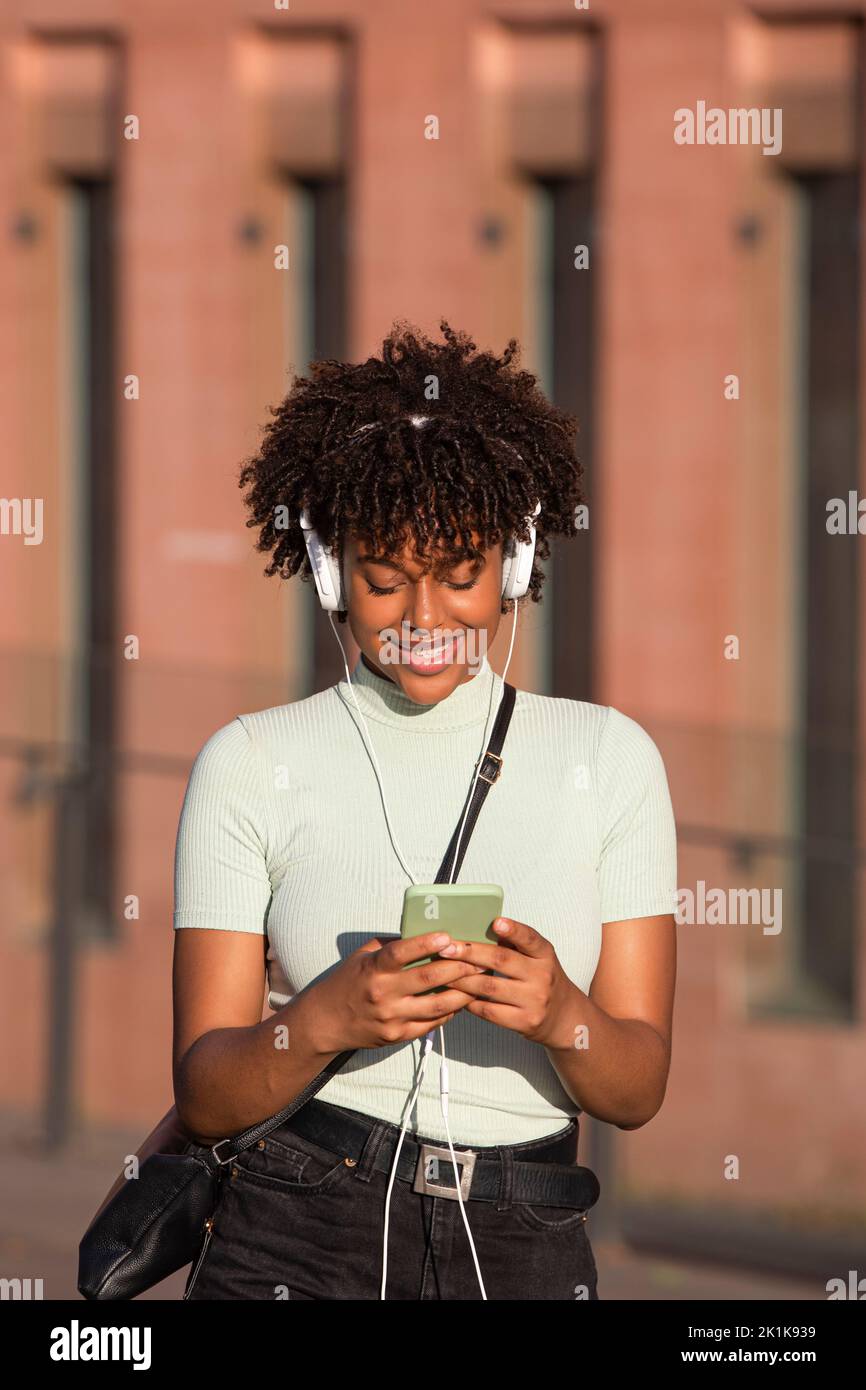 Lächelnde lateinamerikanerin mit Kopfhörern hört Musik auf dem Smartphone Stockfoto