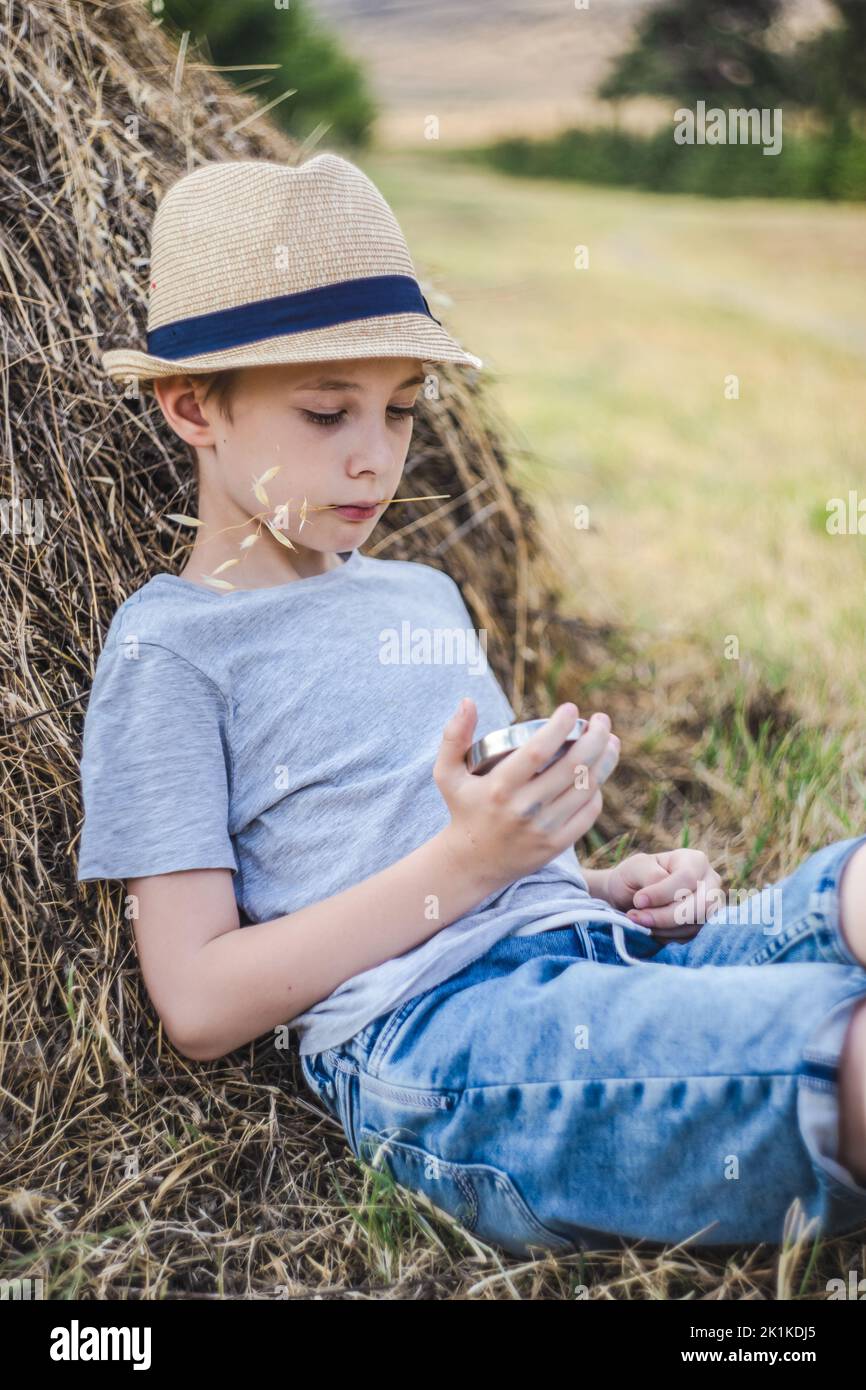 Porträt eines Jungen, der sich an einem Heuhaufen lehnt, ein Stück Stroh kaut und einen Kompass anschaut, Georgia Stockfoto