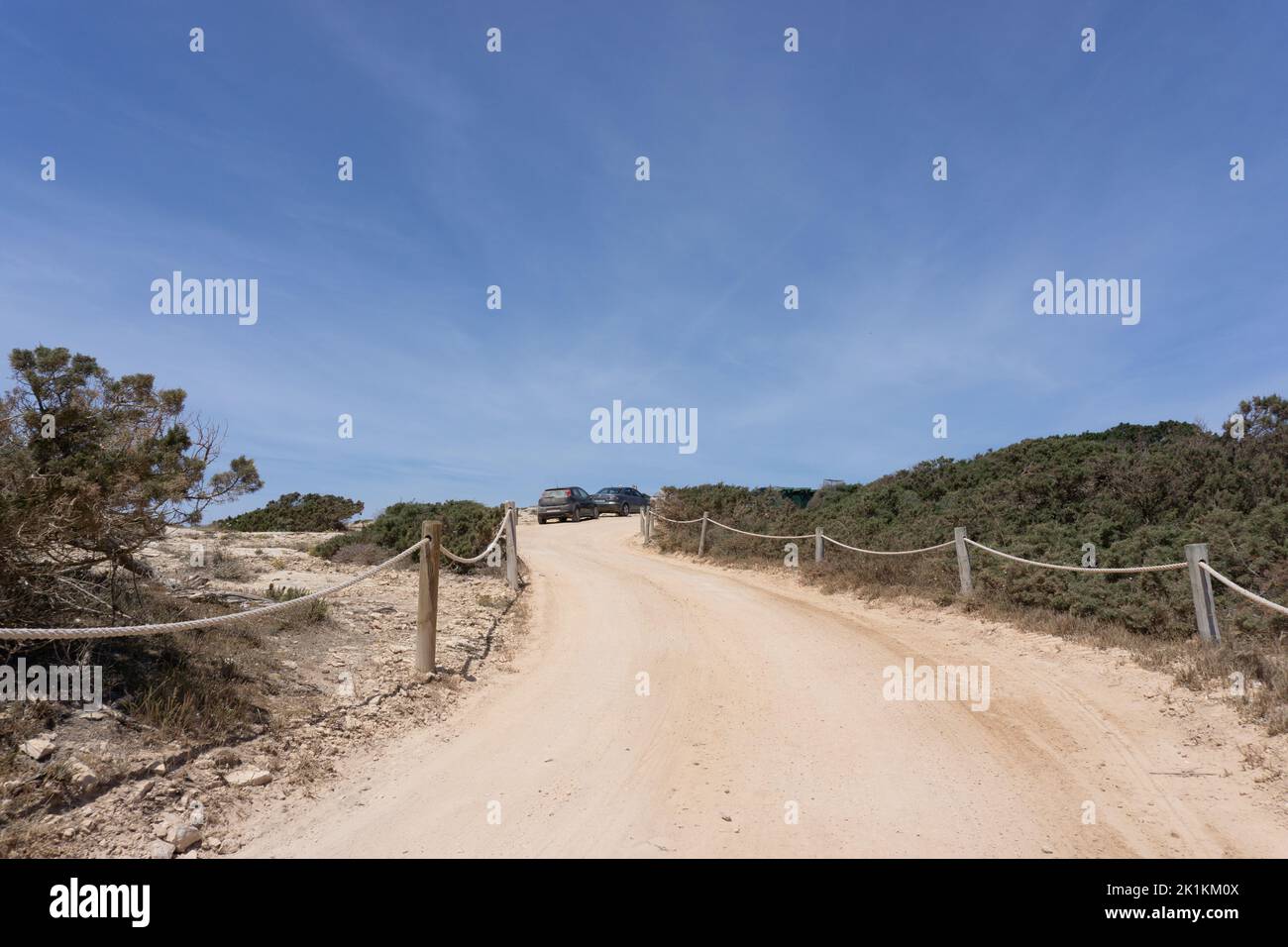 Blick auf Fahrzeuge, die am Rande einer unbefestigten Straße unter dem blauen Himmel auf der Insel Formentera geparkt sind Stockfoto