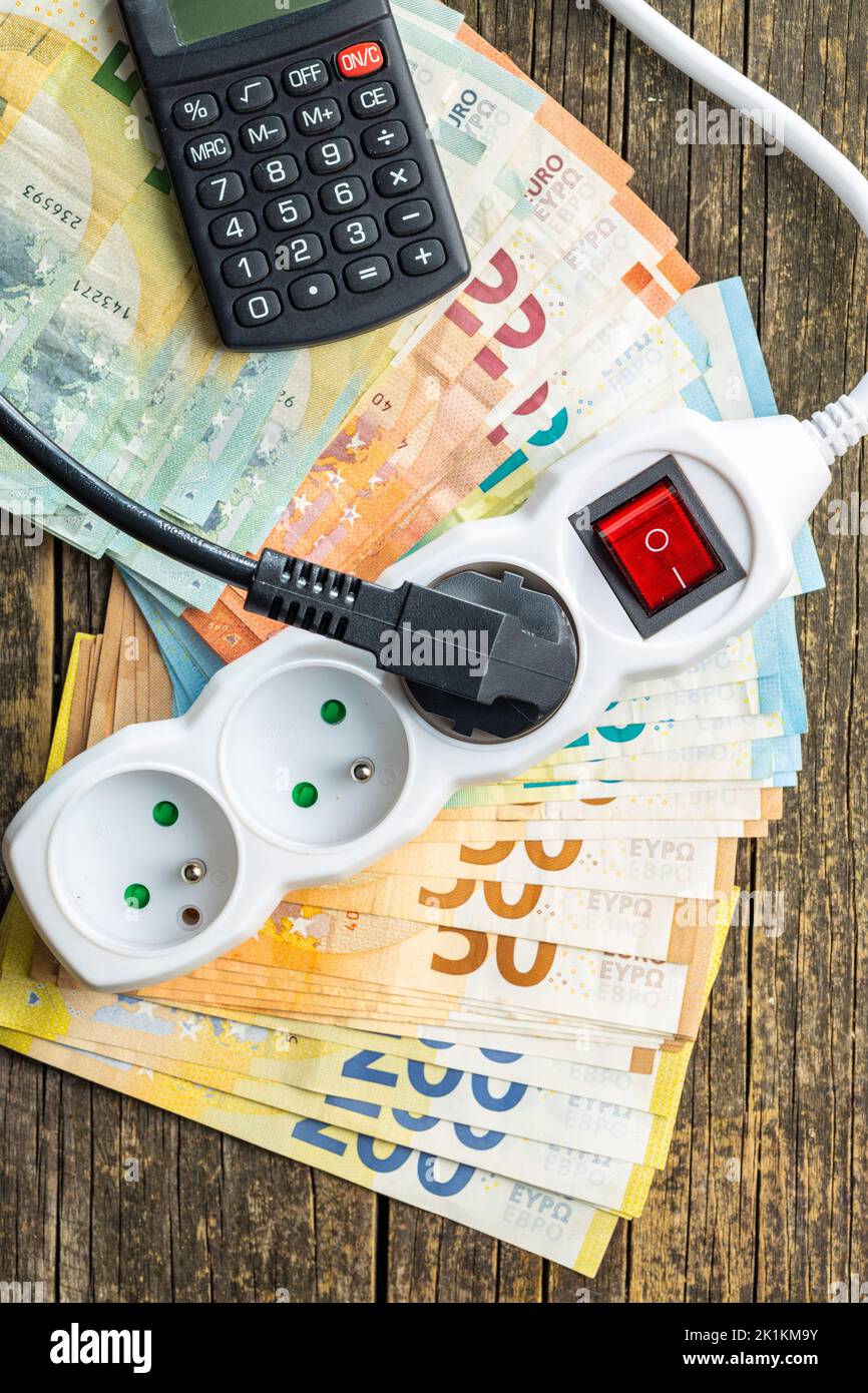 Stecker, Rechner und Euro-Geld auf dem Holztisch. Konzept der steigenden Strompreise. Draufsicht. Stockfoto