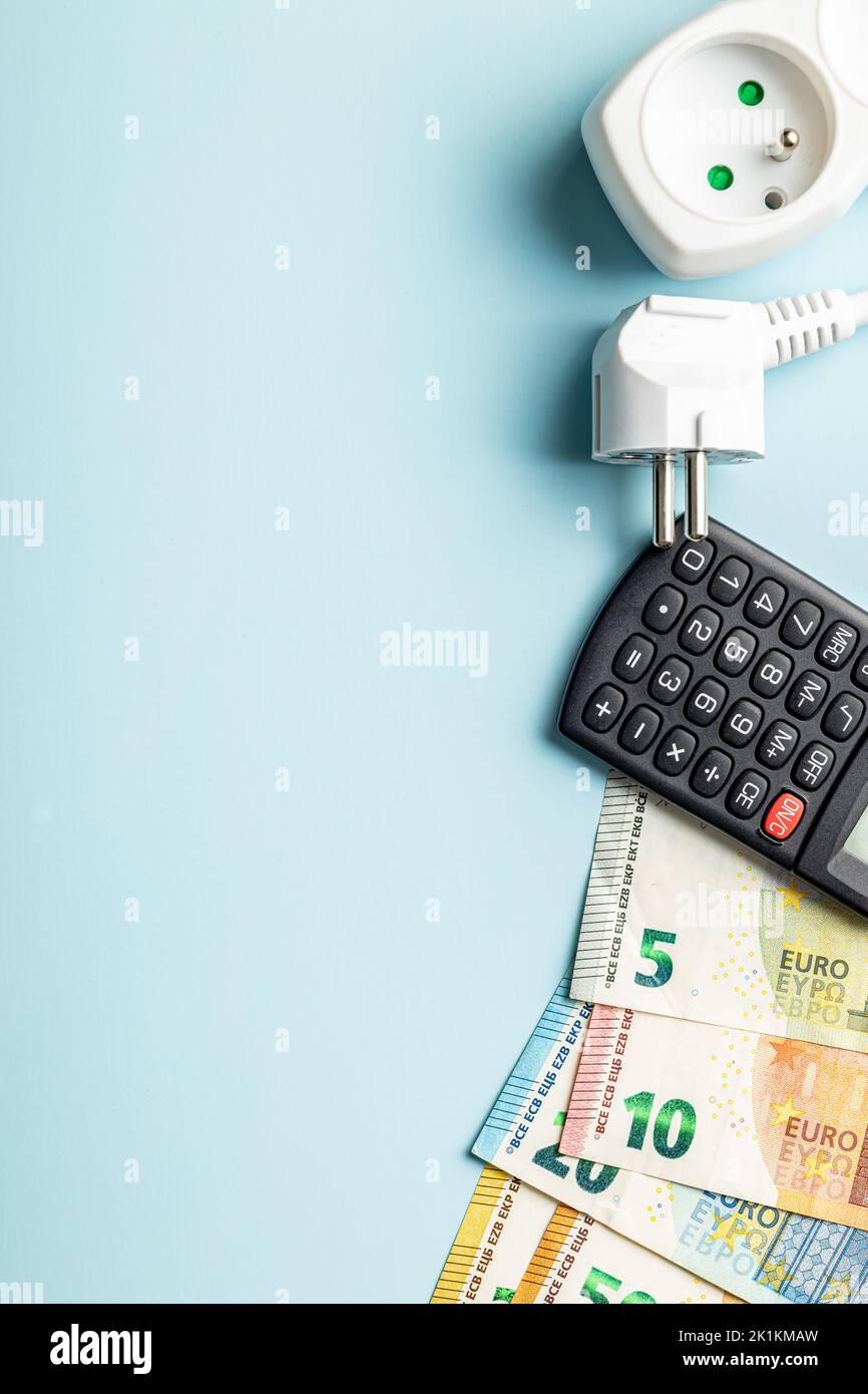 Steckdose, Rechner und Euro-Geld auf blauem Hintergrund. Konzept der steigenden Strompreise. Draufsicht. Stockfoto