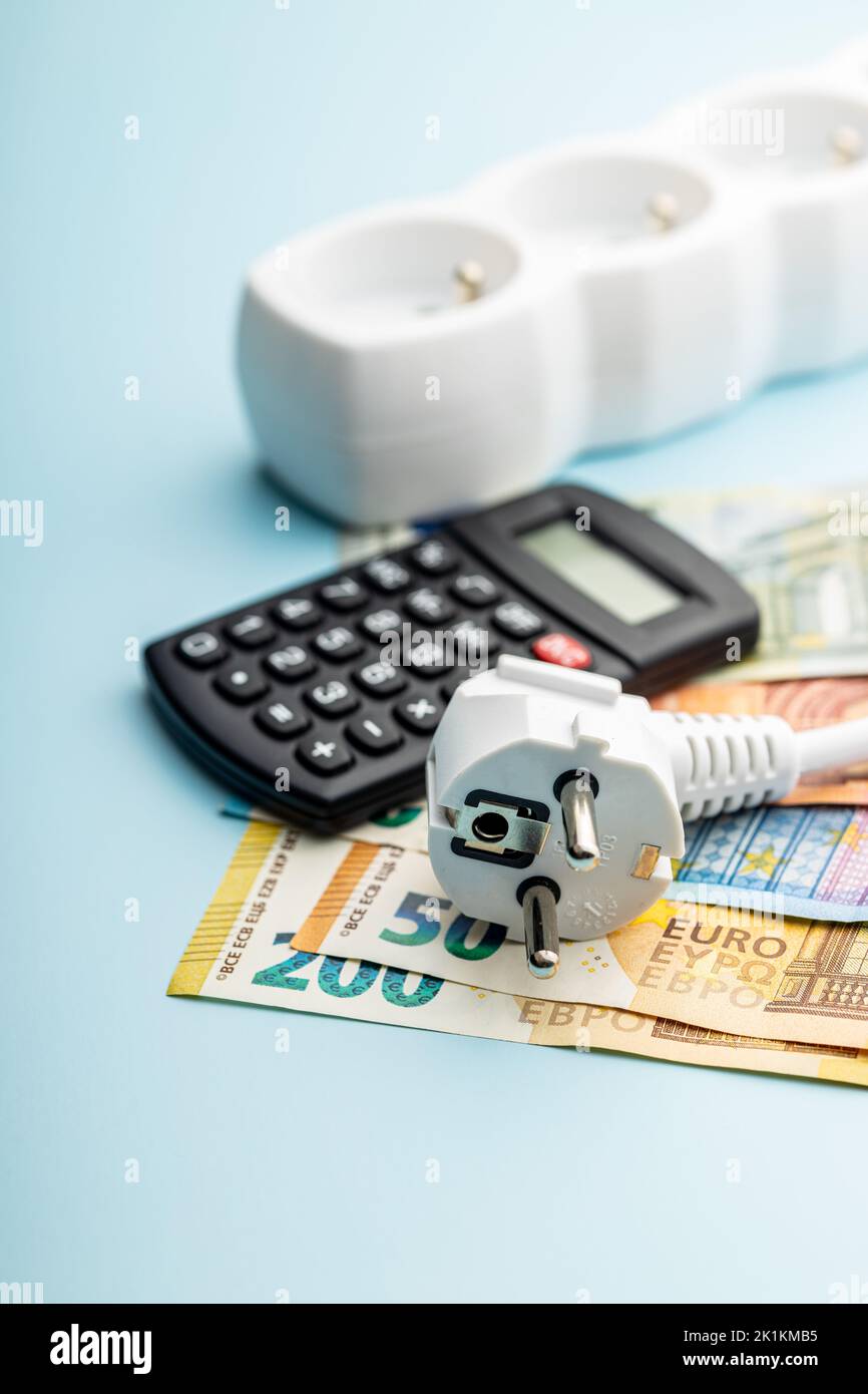 Stecker, Rechner und Euro-Geld auf blauem Hintergrund. Konzept der steigenden Strompreise. Stockfoto