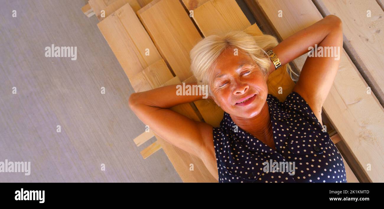 Draufsicht auf glückliche ältere Frau, die an Holzbrettern liegt, breite Fotografie. Speicherplatz kopieren. Stockfoto