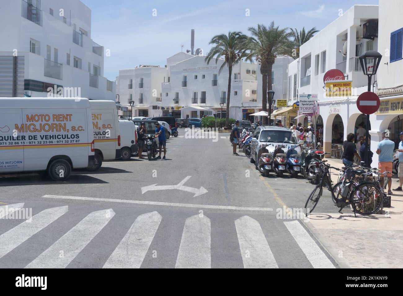 Die Straße, die Fahrzeuge, die Menschen und die weißen Gebäude der Insel Formentera unter dem blauen Himmel Stockfoto