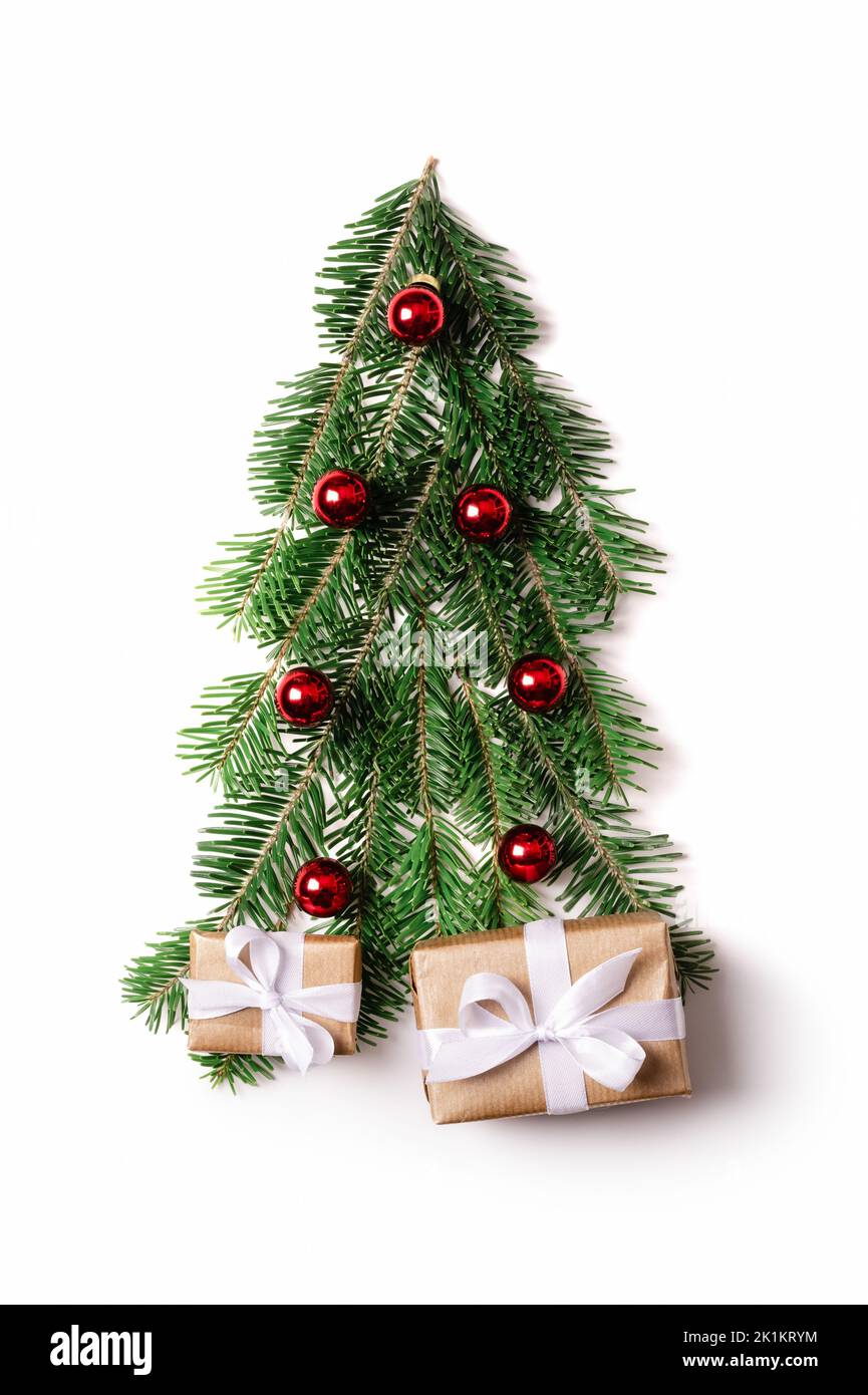 Dekorierter Weihnachtsbaum aus Tannenzweigen mit roten weihnachtskugeln und Geschenken für Neujahr isoliert auf weißem Hintergrund. Geschenkschachteln mit weißen Bändern unter dem Weihnachtsbaum Stockfoto