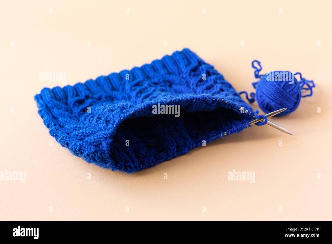 Blaue warme Kleidung mit Stricknadeln und blauen Fadenkugeln auf orangefarbenem Hintergrund stricken Stockfoto